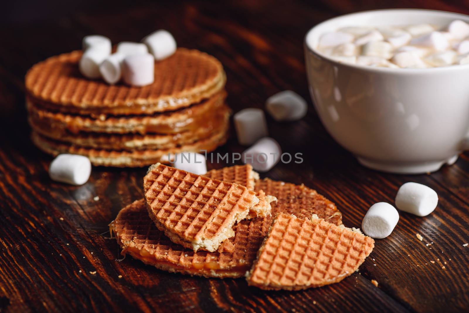Stroopwafel with Broken One with White Cup of Cocoa with Marshmallow and Waffle Stack on Backdrop.