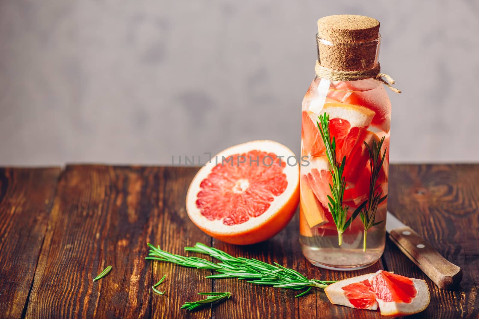 Cleansing Water with Sliced Raw Grapefruit and Fresh Springs of Rosemary. Ingredients and Knife on Wooden Table. Copy Space on the Laft.