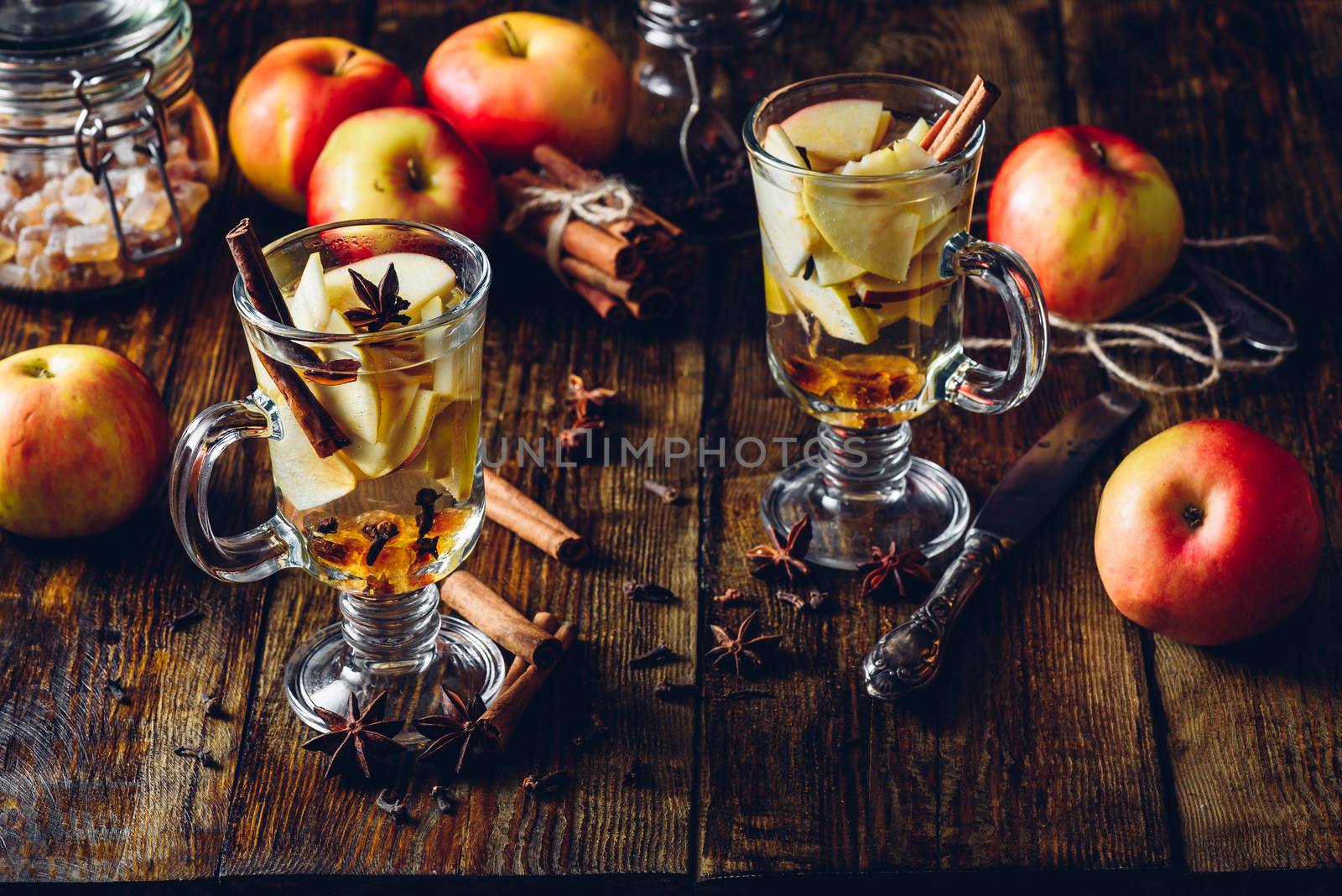Glasses of Apple Spiced Drink with Clove, Cinnamon, Anise Star and Dark Candy Sugar. All Ingredients and Some Kitchen utensils on Wooden Table. Vertical.