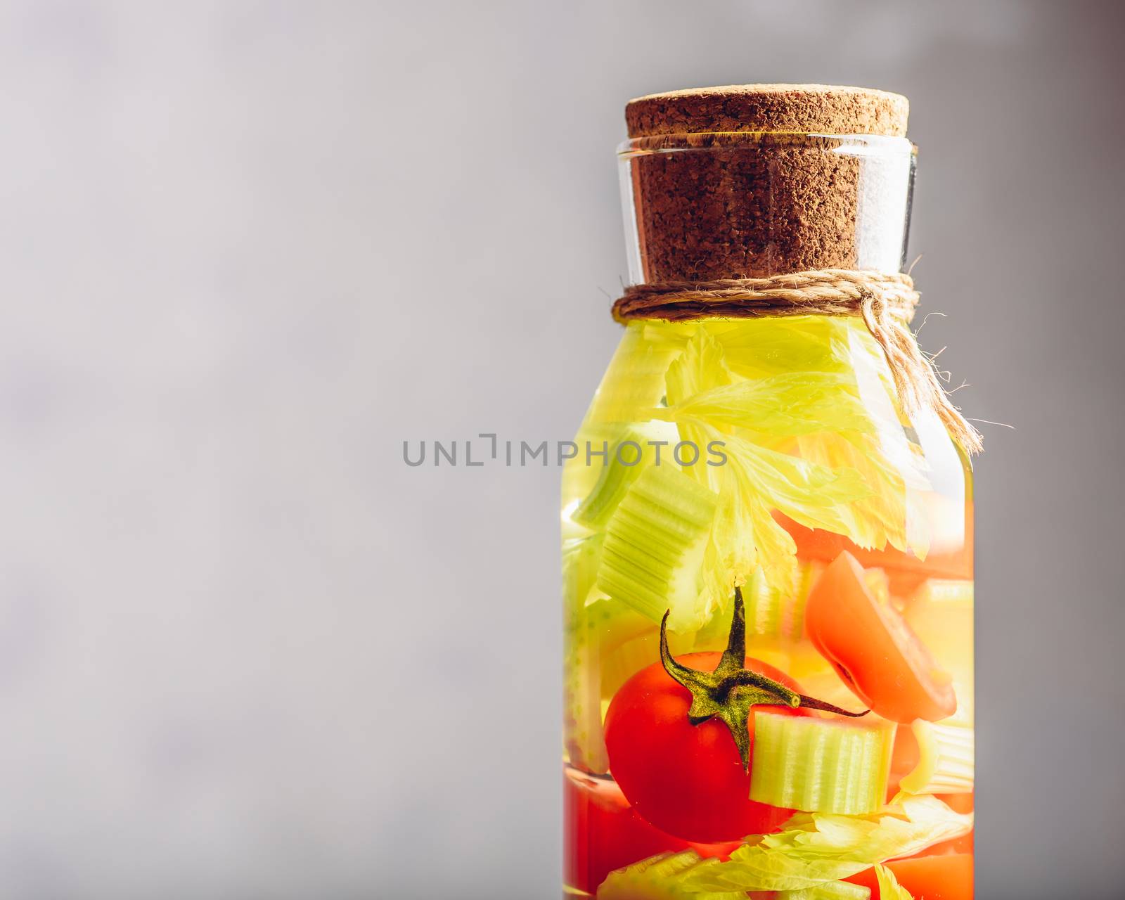 Part of Bottle with Water Infused with Cherry Tomato and Celery Stems. Copy Space on the Left.