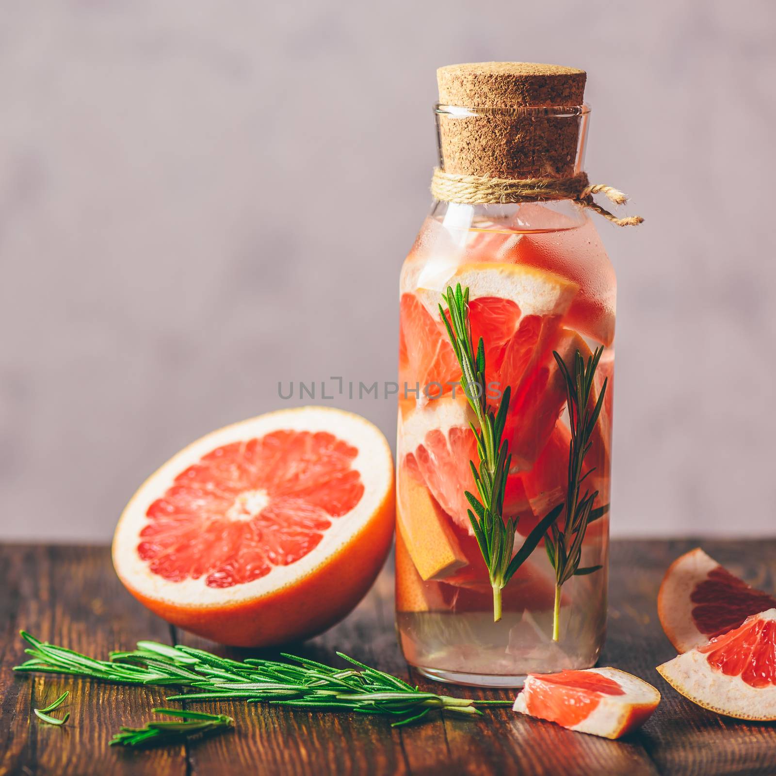 Bottle of Detox Water Infused with Sliced Raw Grapefruit and Fresh Springs of Rosemary. And Ingredients on Wooden Table.