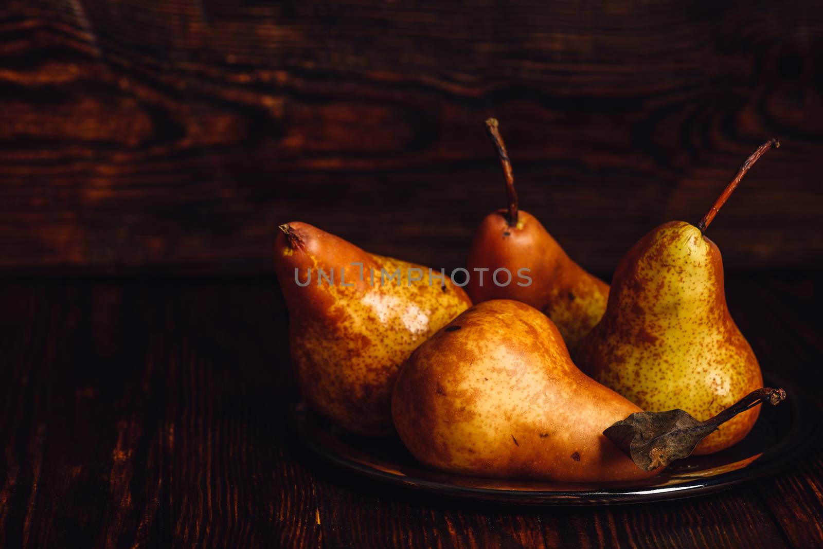 Few golden pears on metal plate over wooden background.