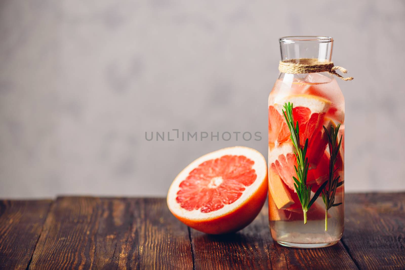 Bottle of Detox Water Infused with Sliced Raw Grapefruit and Fresh Springs of Rosemary and Half of Fruit. Copy Space on the Left Side.