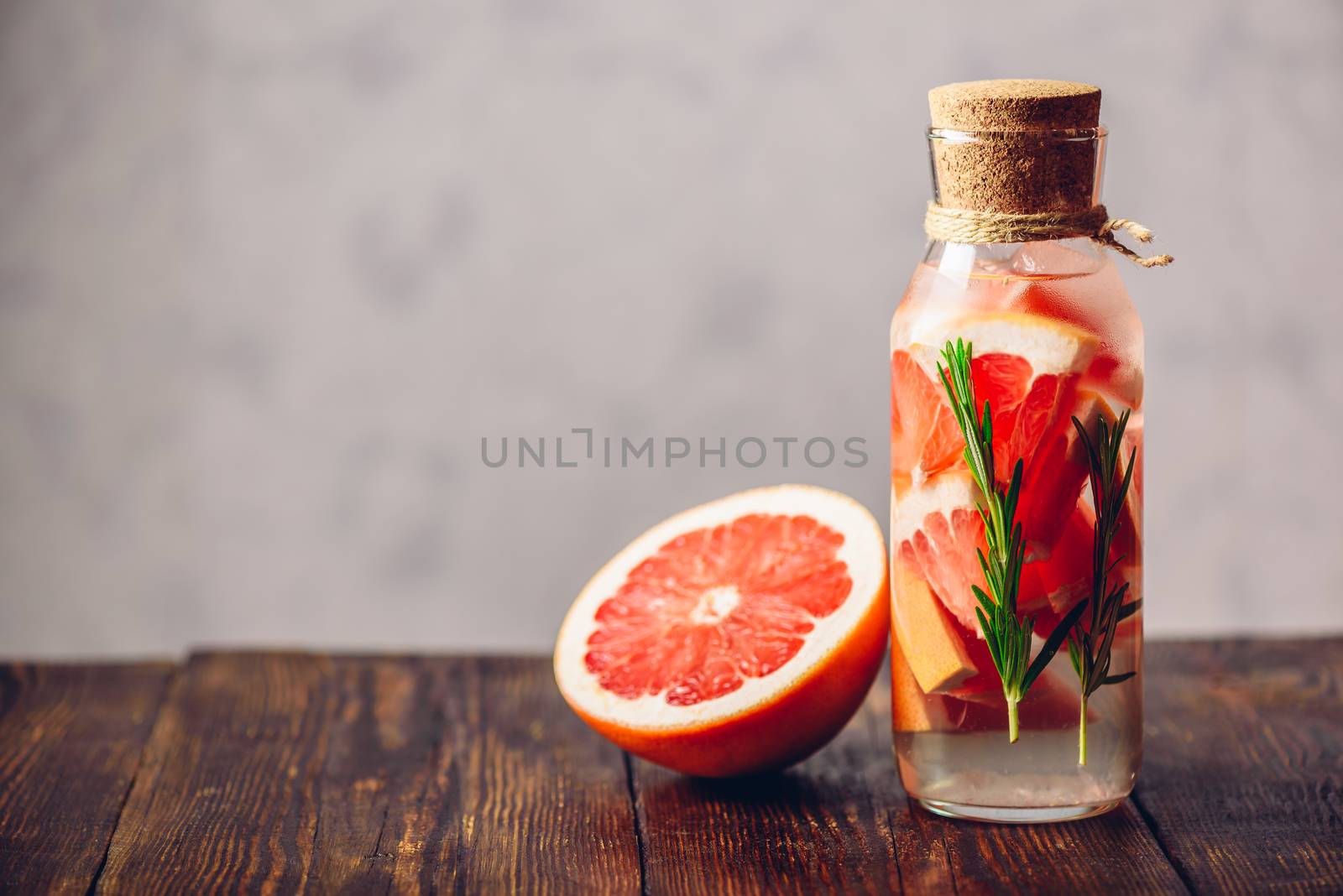 Bottle of Detox Water Infused with Sliced Raw Grapefruit and Fresh Springs of Rosemary and Half of Fruit. Copy Space on the Left Side.