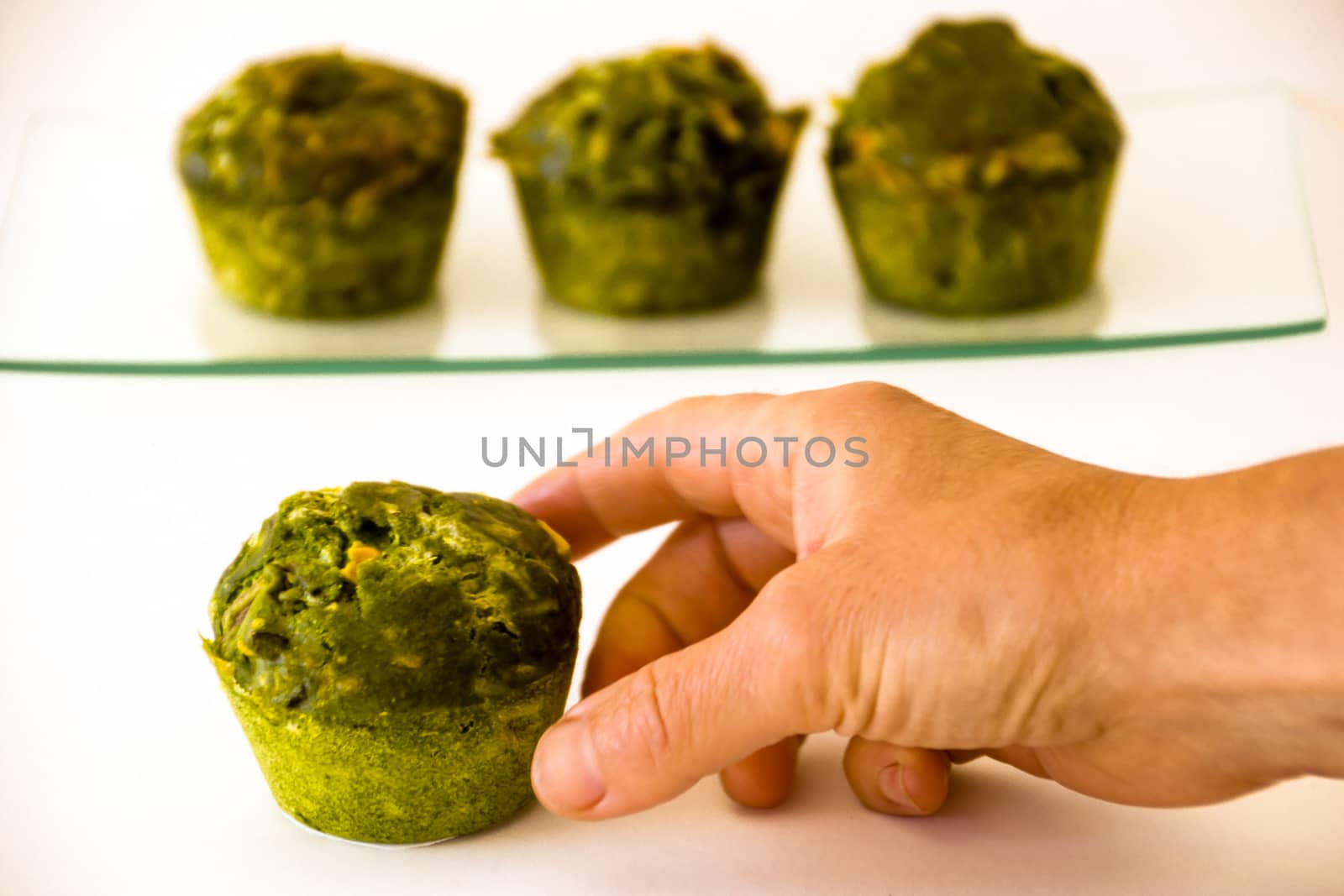 Three green muffins on a glass tray at the background and a hand catching another one at the foreground