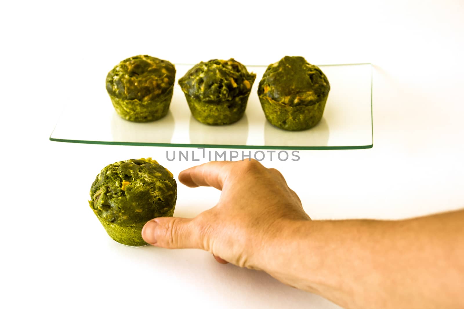 a hand trying to catch a green cake at the foreground and three cakes on a glass tray at the background