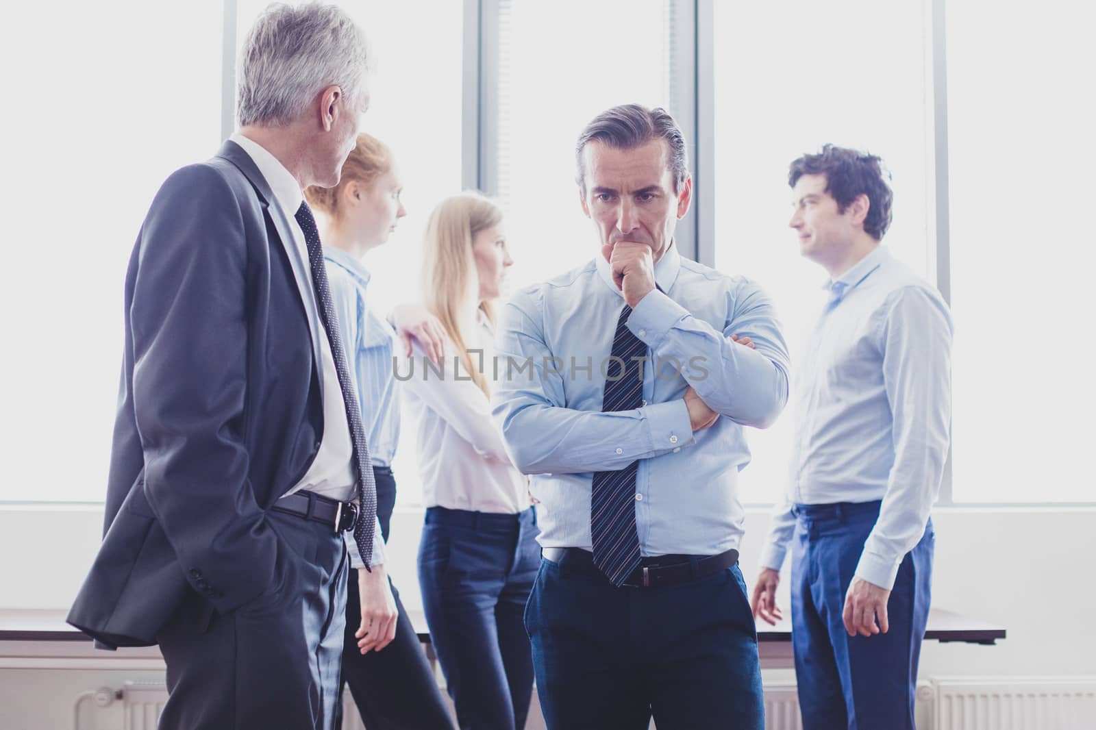 Colleagues having business conversation at meeting in office, serious man thinking holding chin