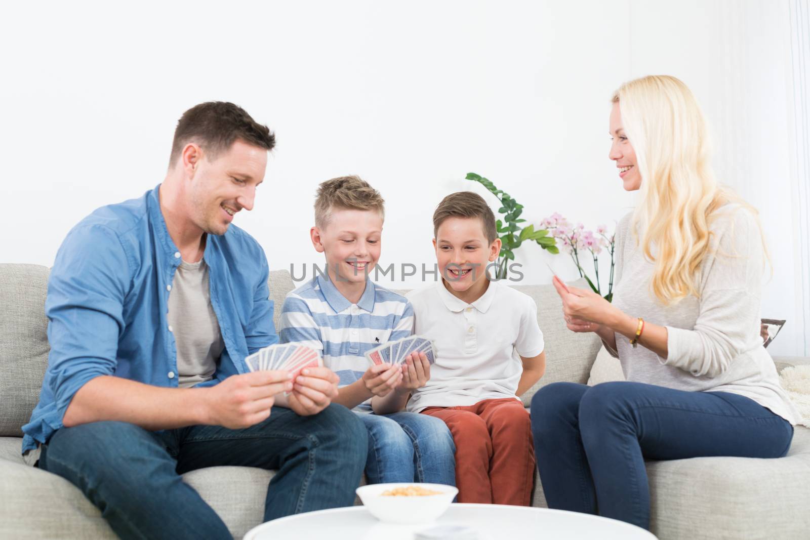 Happy young family playing card game on living room sofa at home. Spending quality leisure time with children and family concept. Cards are generic and debranded.