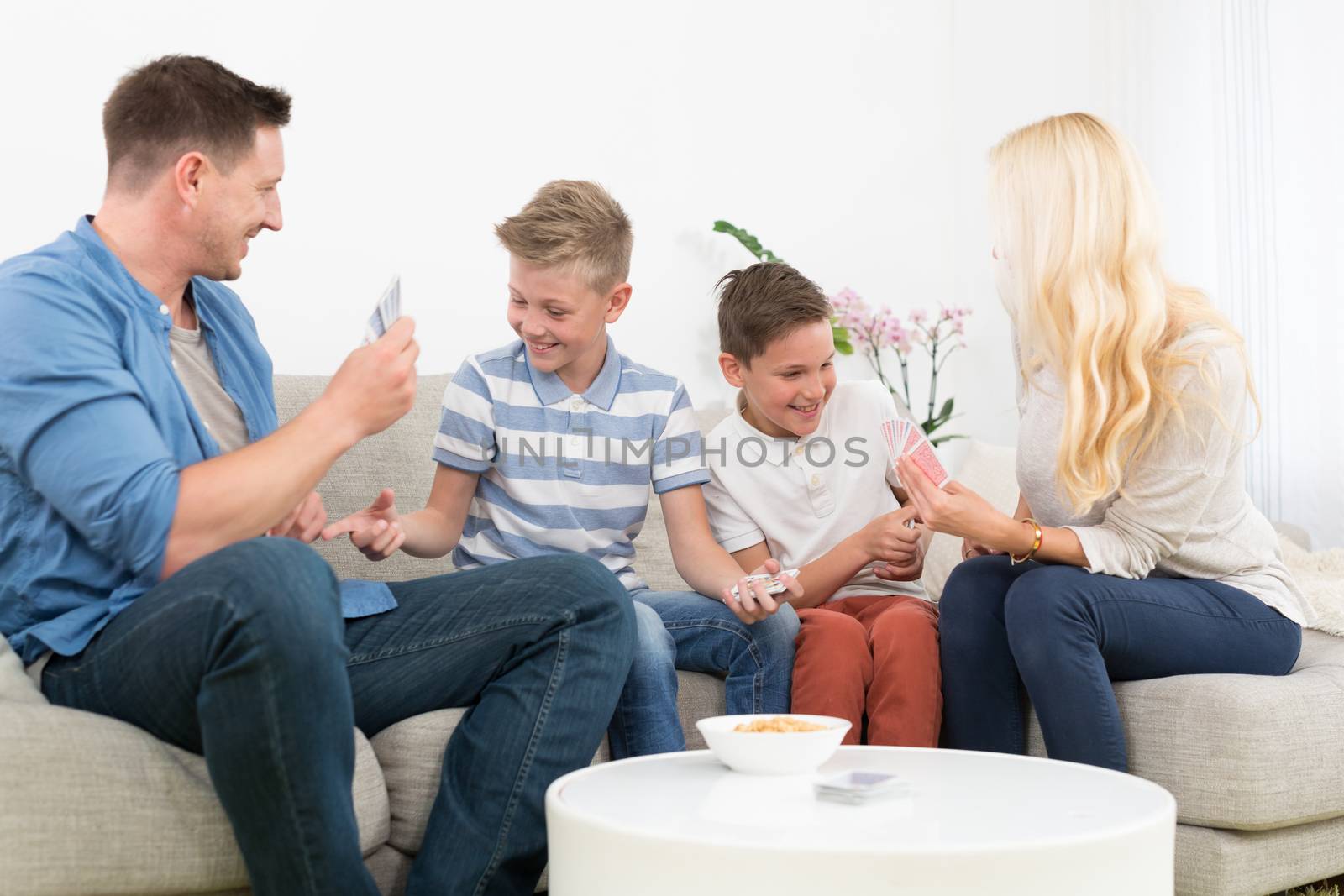 Happy young family playing card game on living room sofa at home. Spending quality leisure time with children and family concept. Cards are generic and debranded.