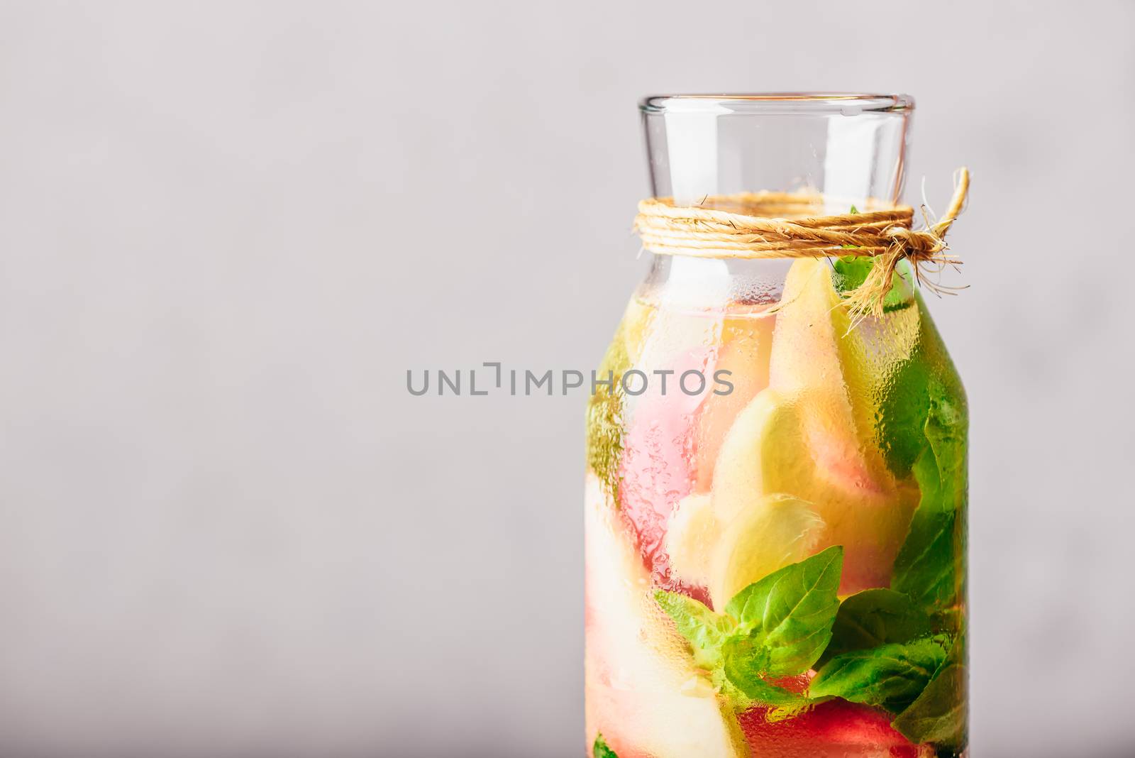 Part of Bottle of Infused Water with Sliced Peach and Basil Leaves.