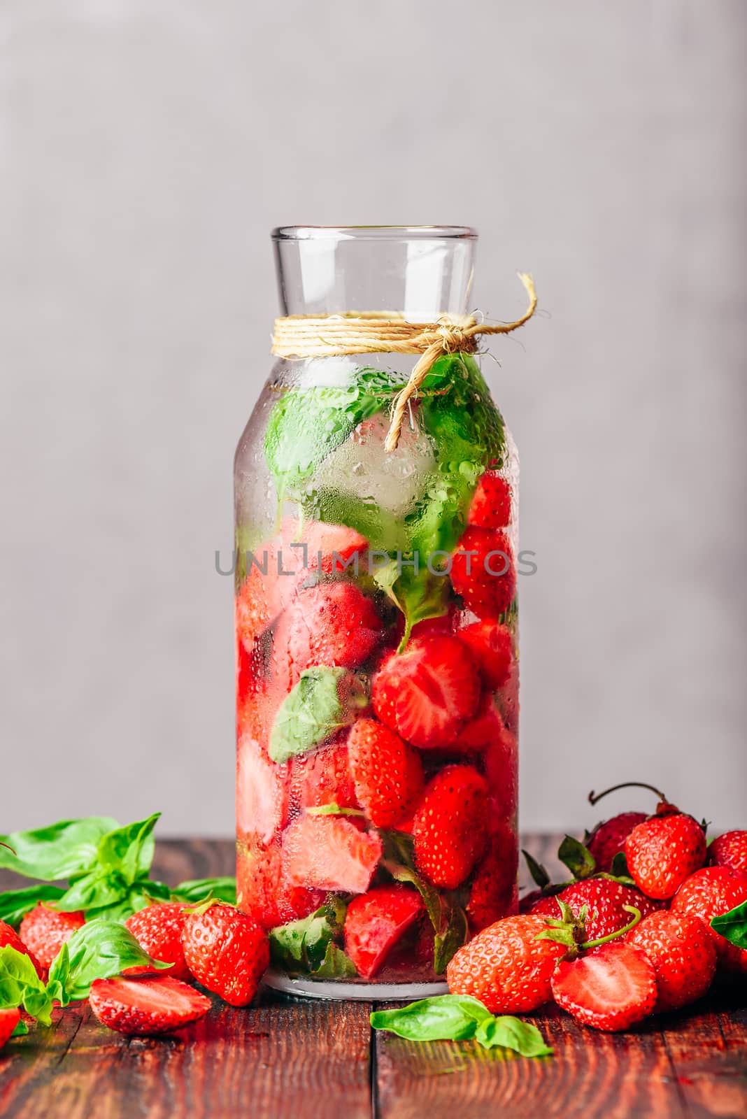 Bottle of Water Infused with Fresh Strawberry and Basil Leaves. Scattered Ingredients on Wooden Table. Vertical Orientation and Copy Space.