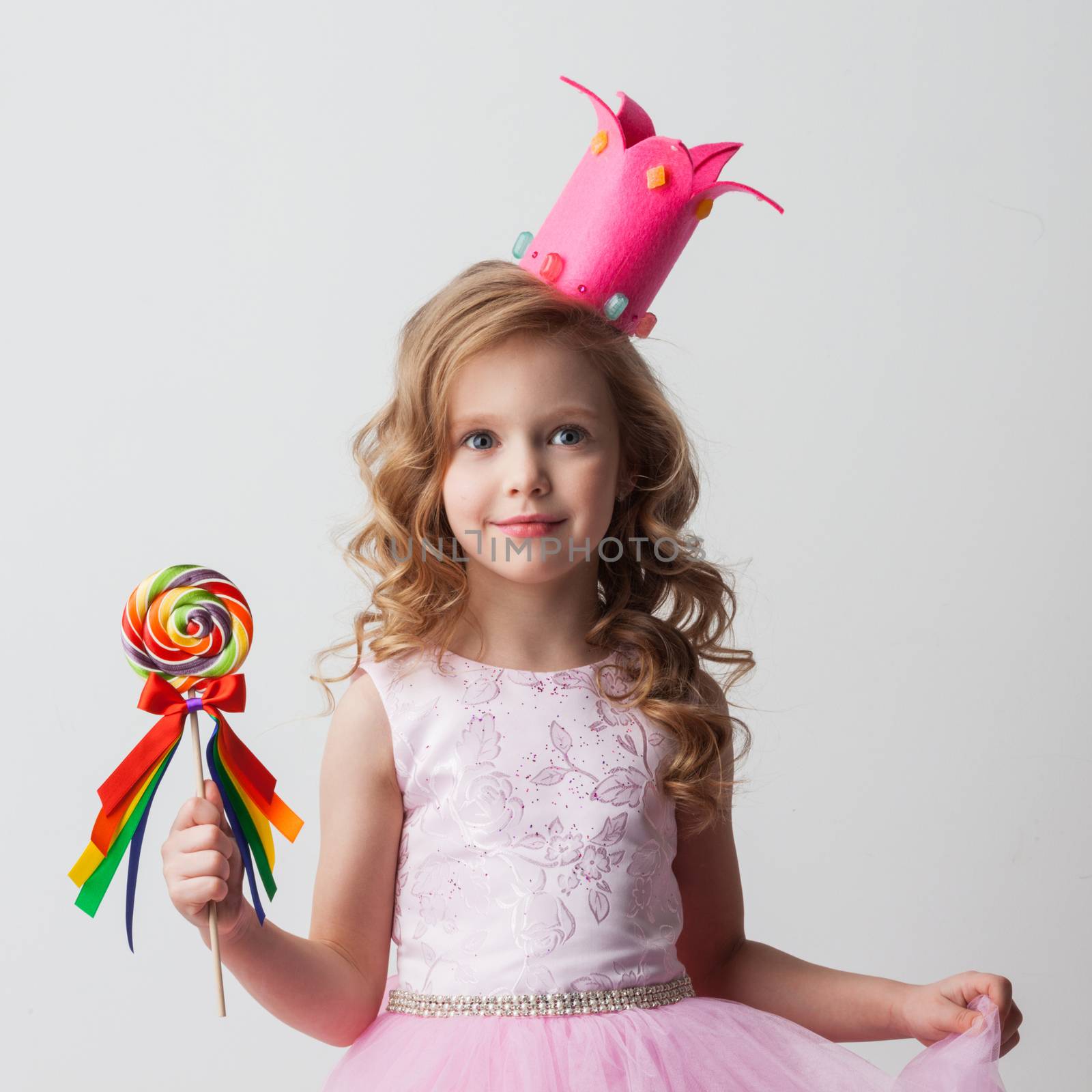 Beautiful little candy princess girl in crown holding big lollipop and smiling