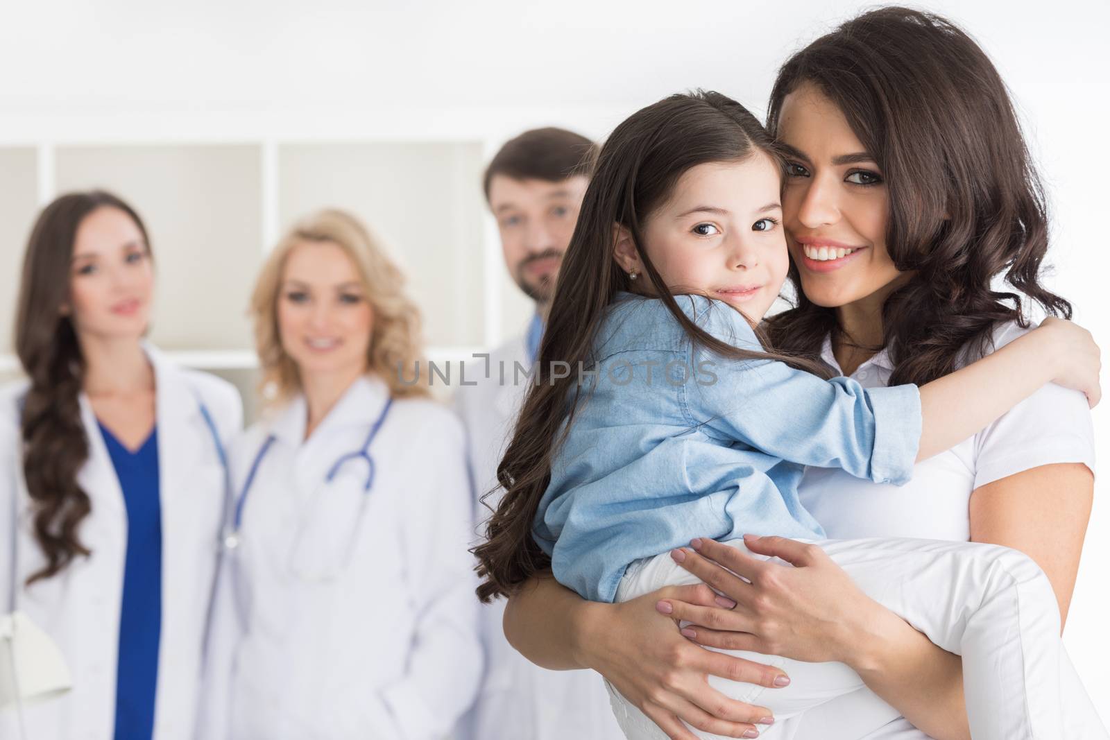 Mother and daughter in medical clinic, team of doctors on background