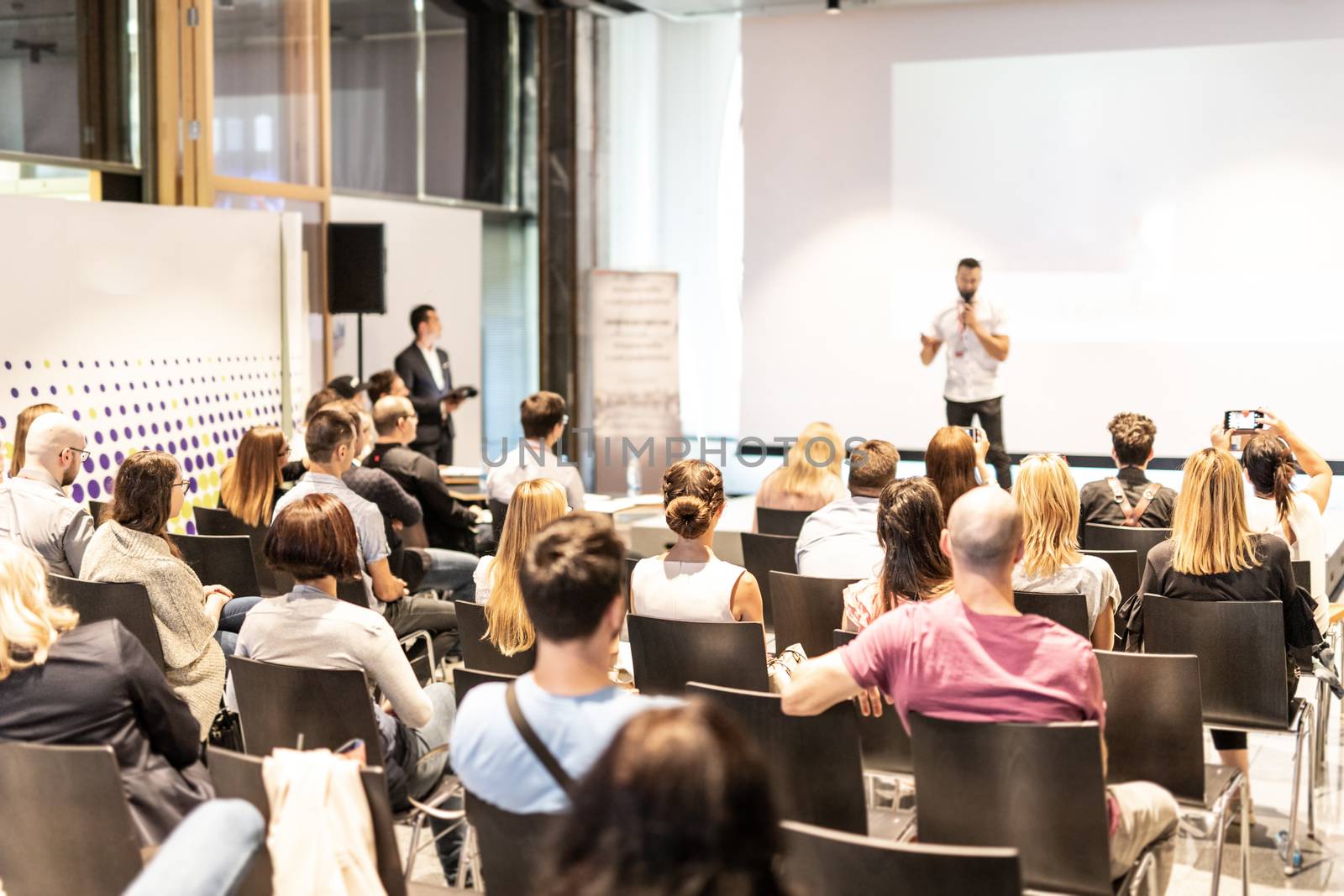 Male speaker giving a talk in conference hall at business event. Audience at the conference hall. Business and Entrepreneurship concept. Focus on unrecognizable people in audience.