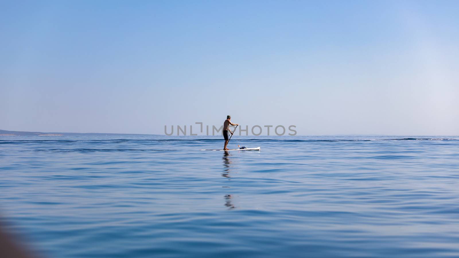 A standup paddleboarding, supsurfing man in the Adriatic sea in Croatia