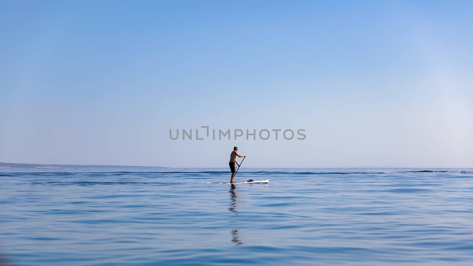 A standup paddleboarding, supsurfing man in the Adriatic sea in Croatia