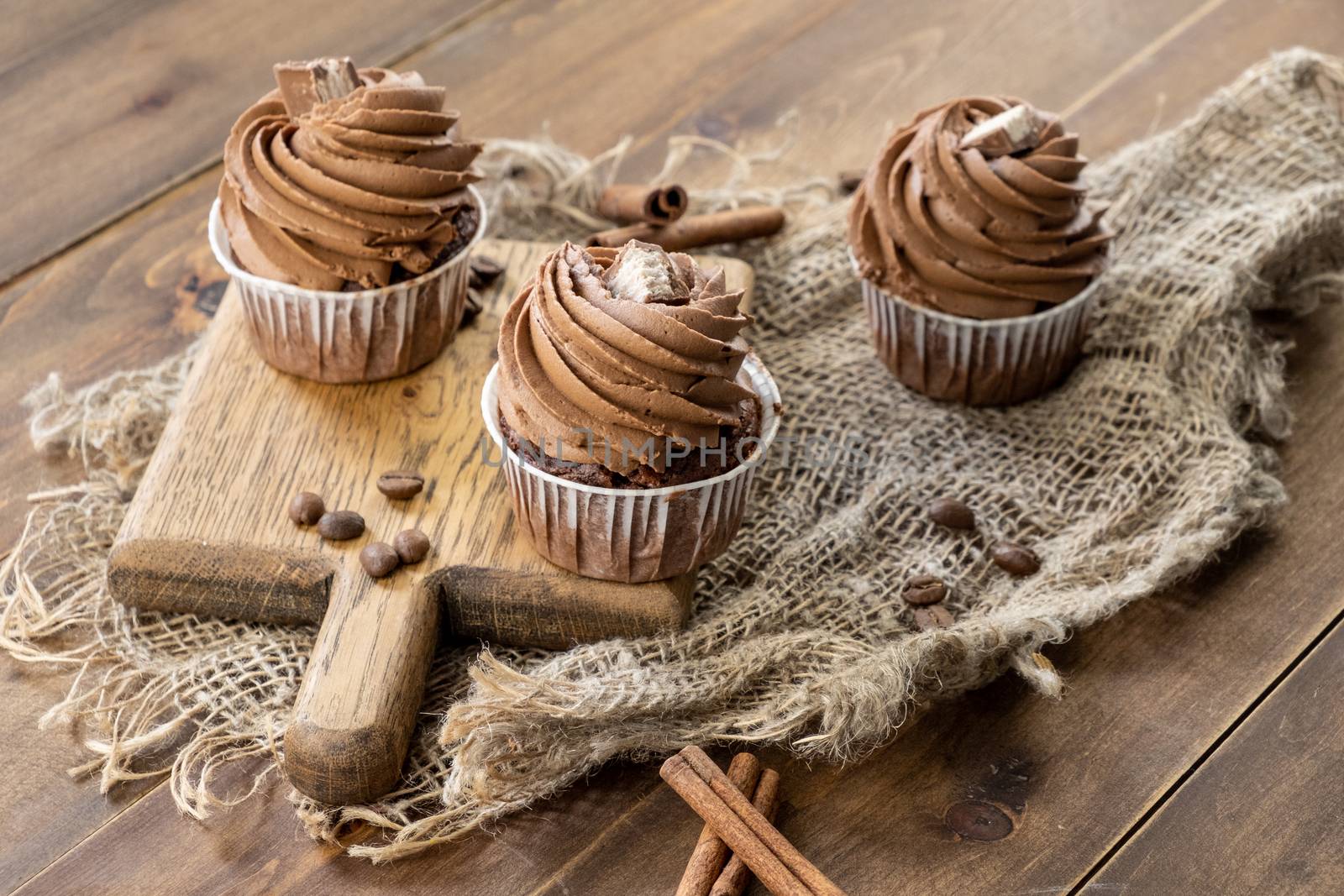 brown cupcakes with cocoa cream, cinnamon and coffee on wooden background by rdv27