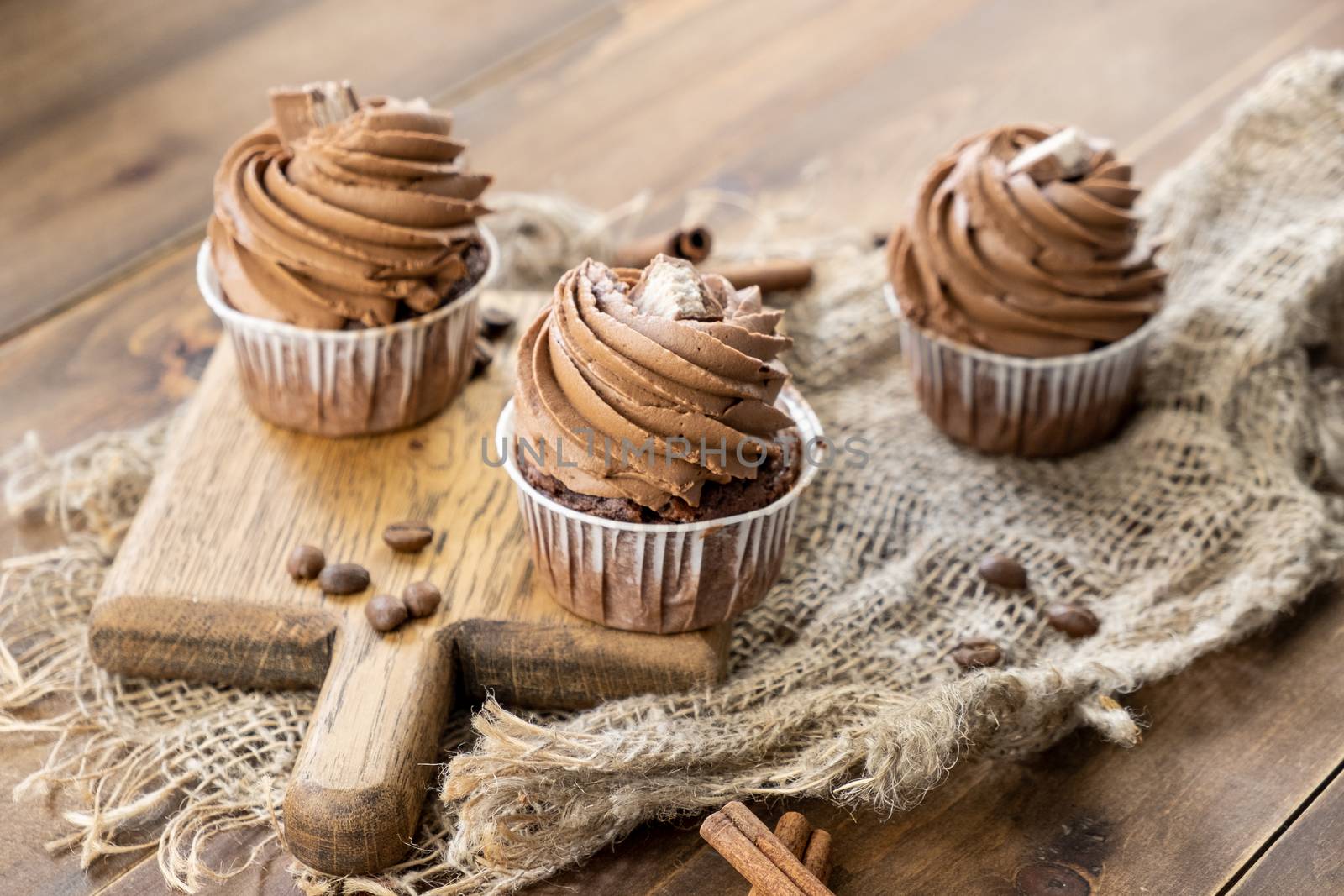 brown cupcakes with cocoa cream, cinnamon and coffee on wooden background by rdv27