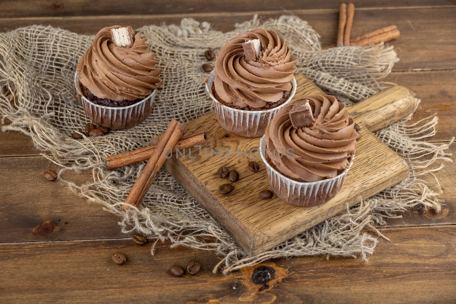 brown cupcakes with cocoa cream, cinnamon and coffee on wooden background by rdv27