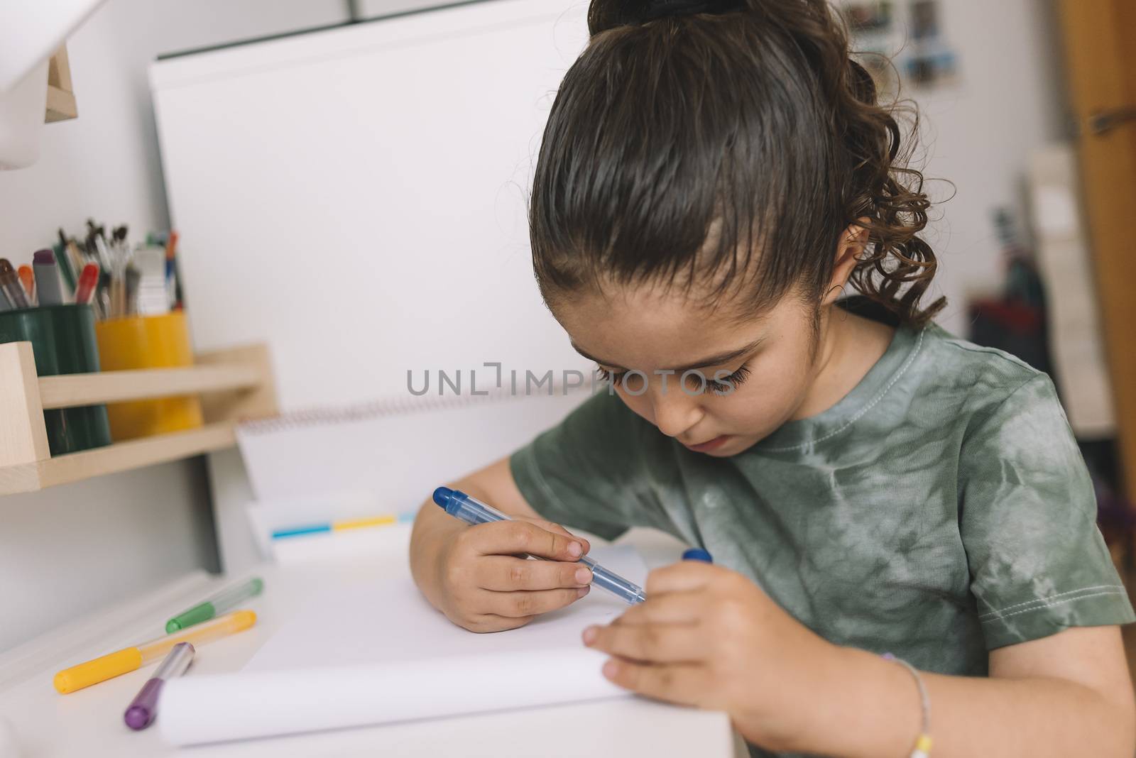 little girl draws at home with colored markers, she is drawing on the desk in her room