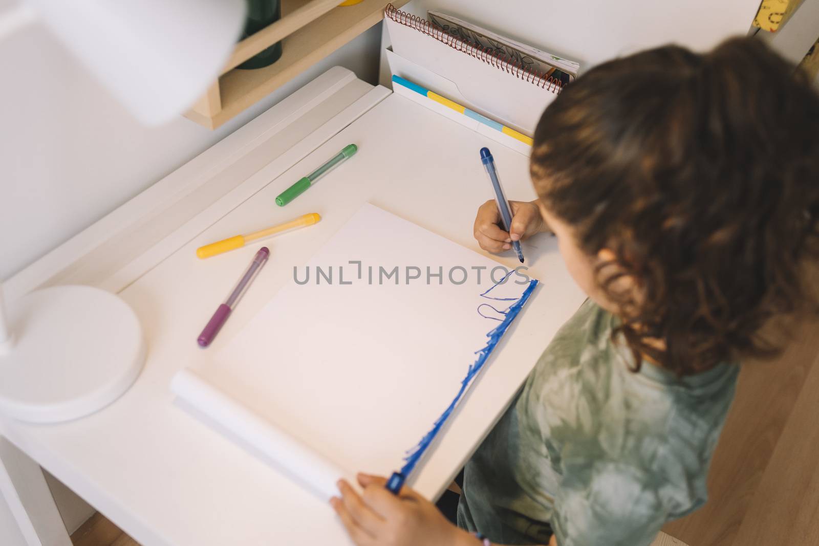 little girl draws at home with color markers, she is drawing on the table in her room