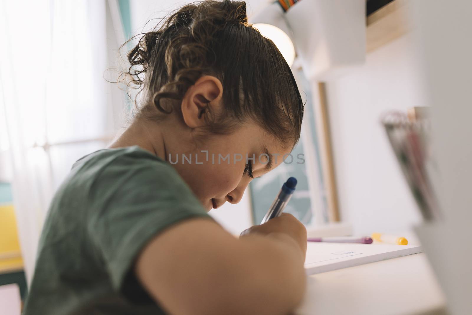 little girl draws concentrated at home with color markers, she is writing on the table in her room