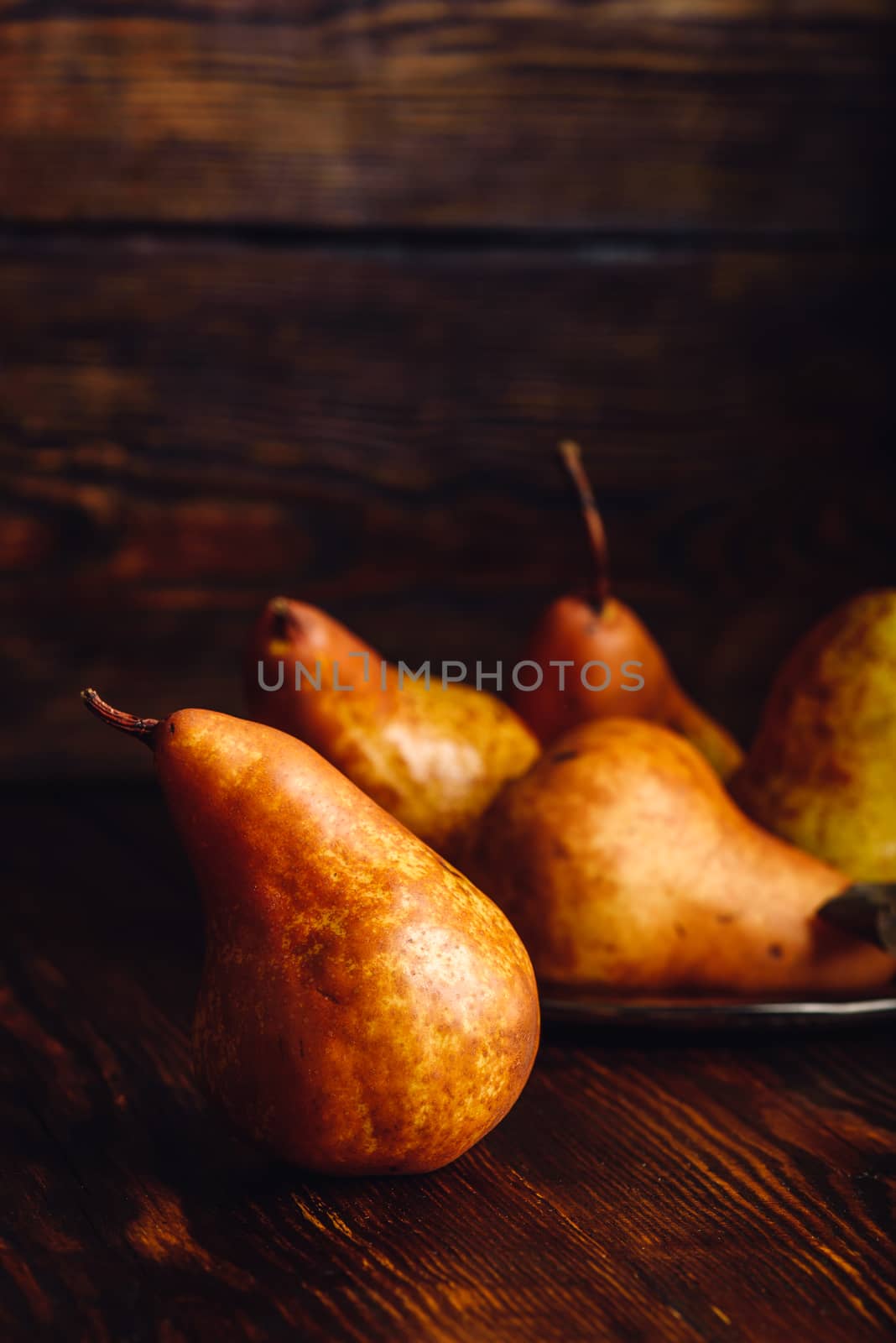 Golden Pear on Wooden Table and Few Pears on Backdrop. Vertical Orientation.