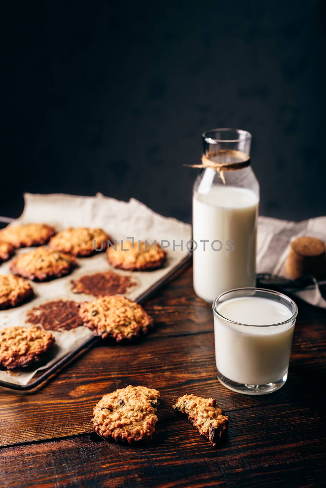 Oatmeal Cookies with Raisins and Glass of Milk for Breakfast. Some Cookies on Parchment Paper with Bottle on Backdrop. Copy Space on the Top.