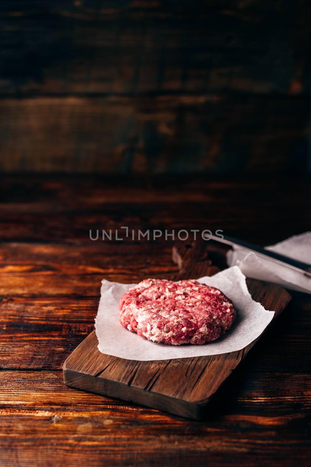 Raw Beef Patty for Burger on Cutting Board and Wax Paper. Vertical Orientation and Copy Space.