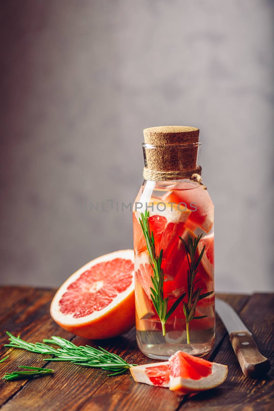 Bottle of Water Infused with Sliced Raw Grapefruit and Fresh Springs of Rosemary. Vertical Orientation. Copy Space on the Top.