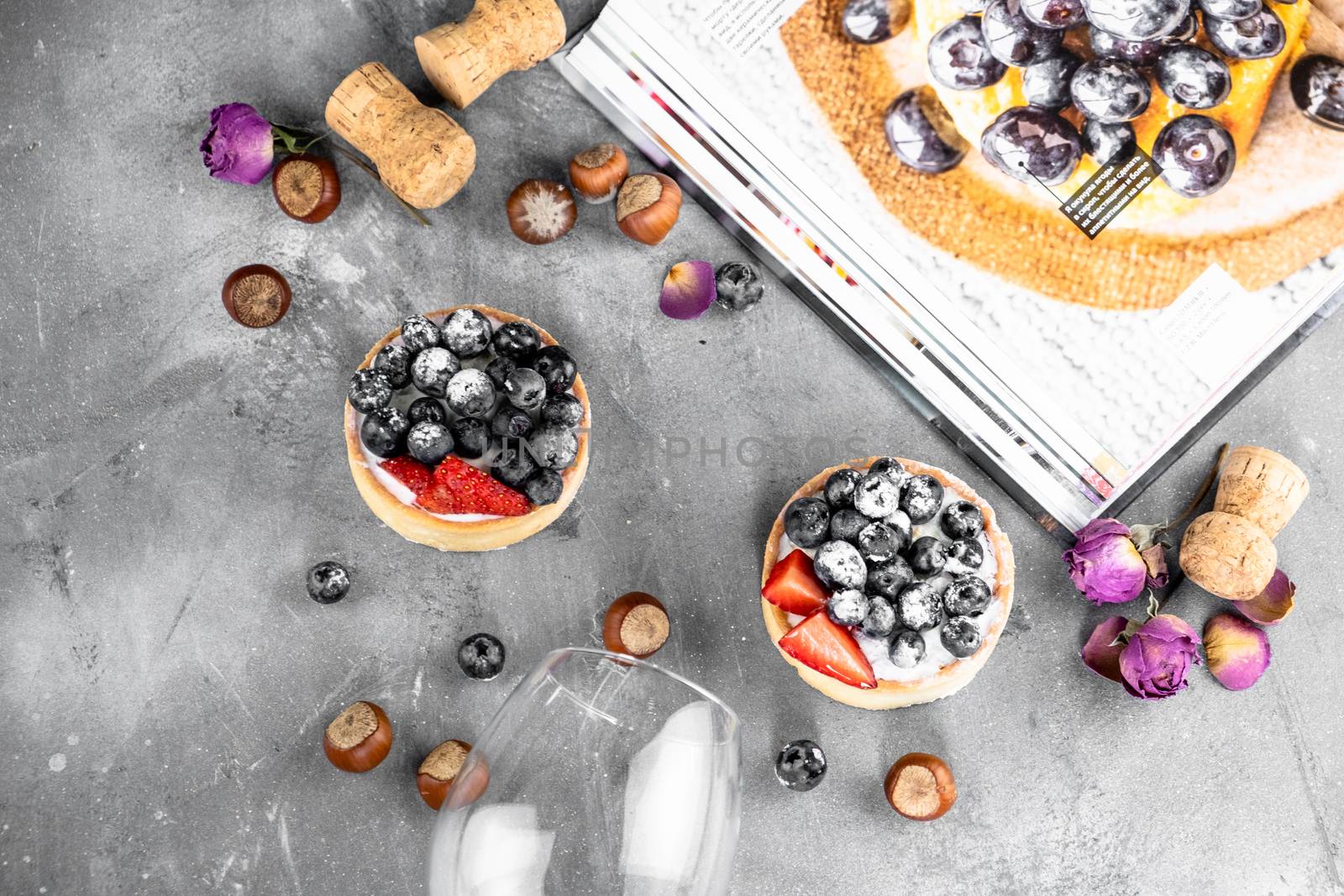 Blueberry and strawberry shortcake. There are hazelnuts, roses and wine corks on the table. Stone gray background.