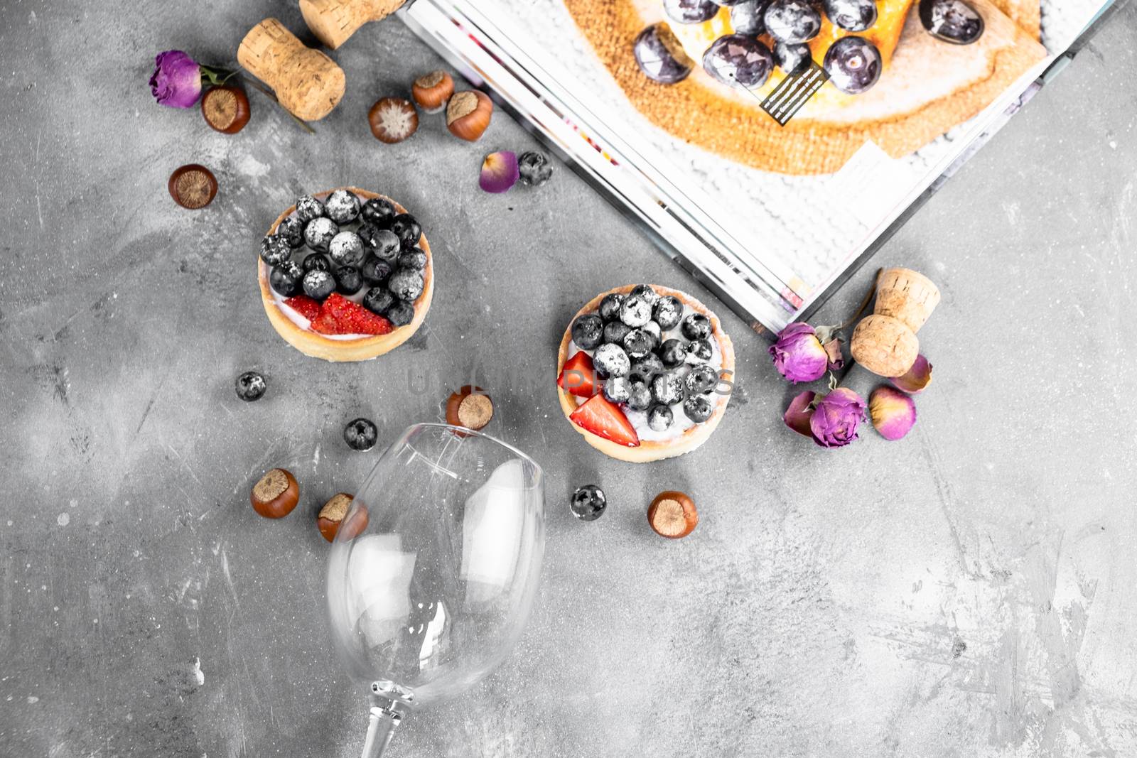 Blueberry and strawberry shortcake. There are hazelnuts, roses and wine corks on the table. Stone gray background.