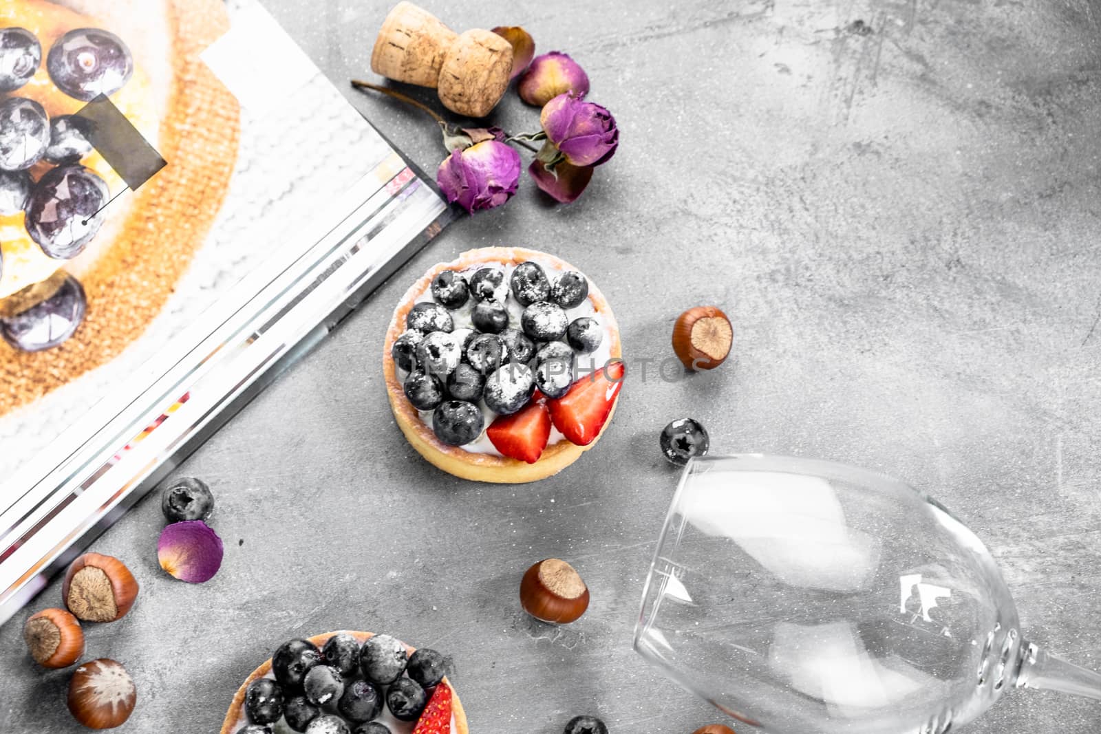 Blueberry and strawberry shortcake. There are hazelnuts, roses and wine corks on the table. Stone gray background.