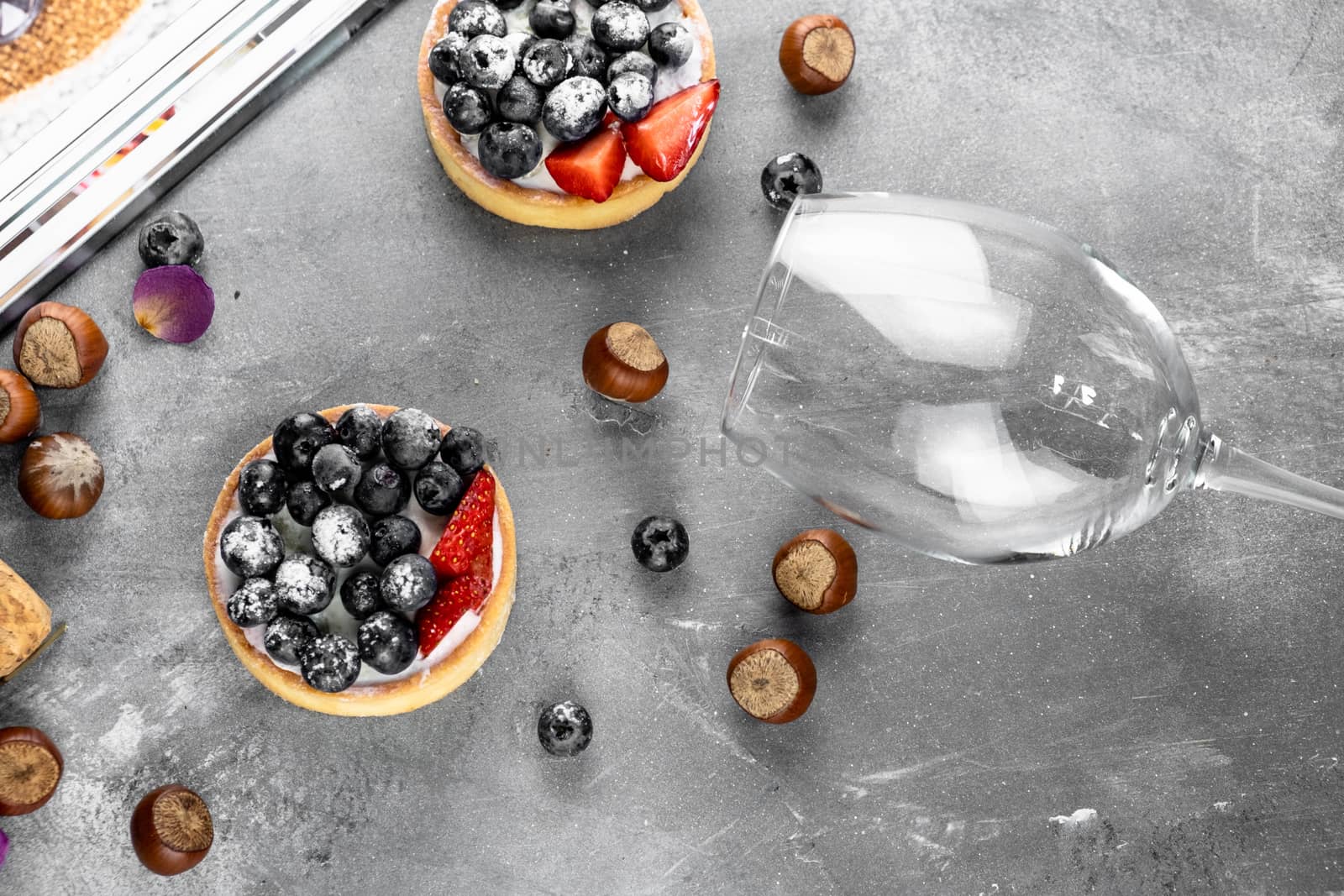 Blueberry and strawberry shortcake. There are hazelnuts, roses and wine corks on the table. Stone gray background.