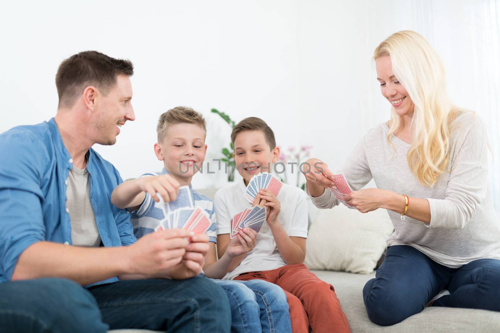 Happy young family playing card game on living room sofa at home. Spending quality leisure time with children and family concept. Playing cards are generic and debranded.