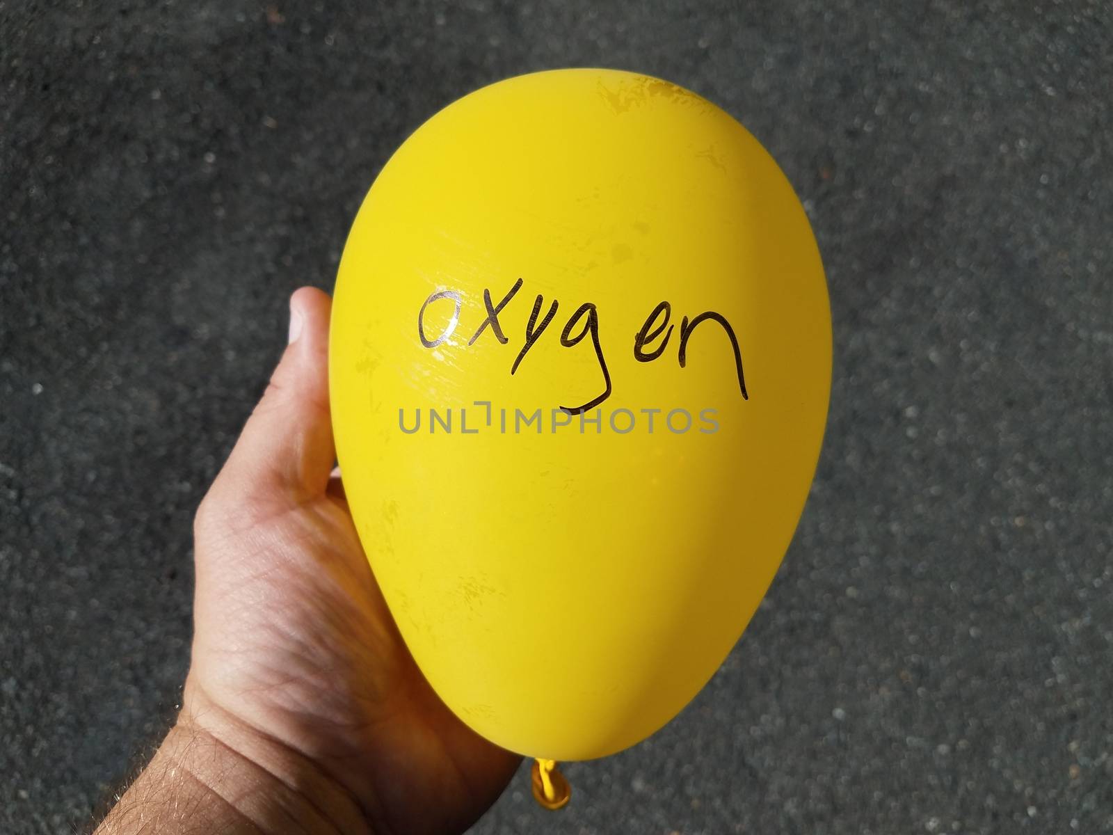 hand holding yellow balloon with oxygen written on it and black asphalt