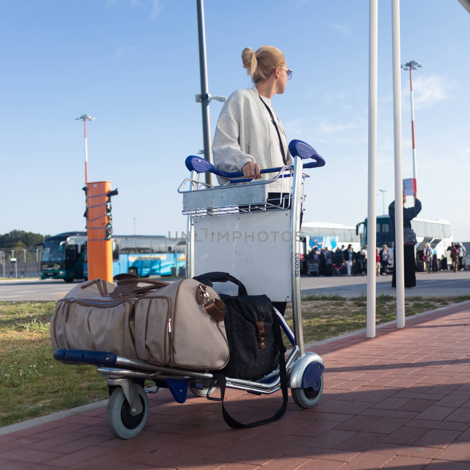 Young woman transporting luggage from arrival parking to international airport departure termainal by luggage trolley. by kasto