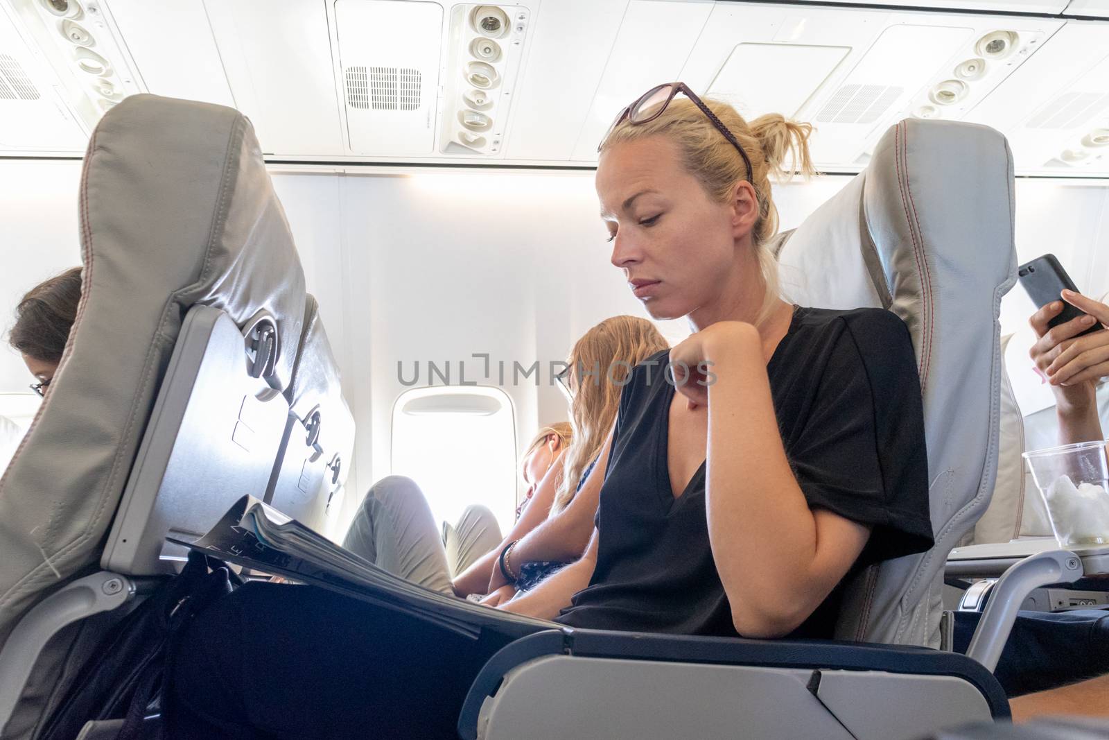 Female traveler reading magazine on airplane during flight. Female traveler reading seated in passanger cabin.