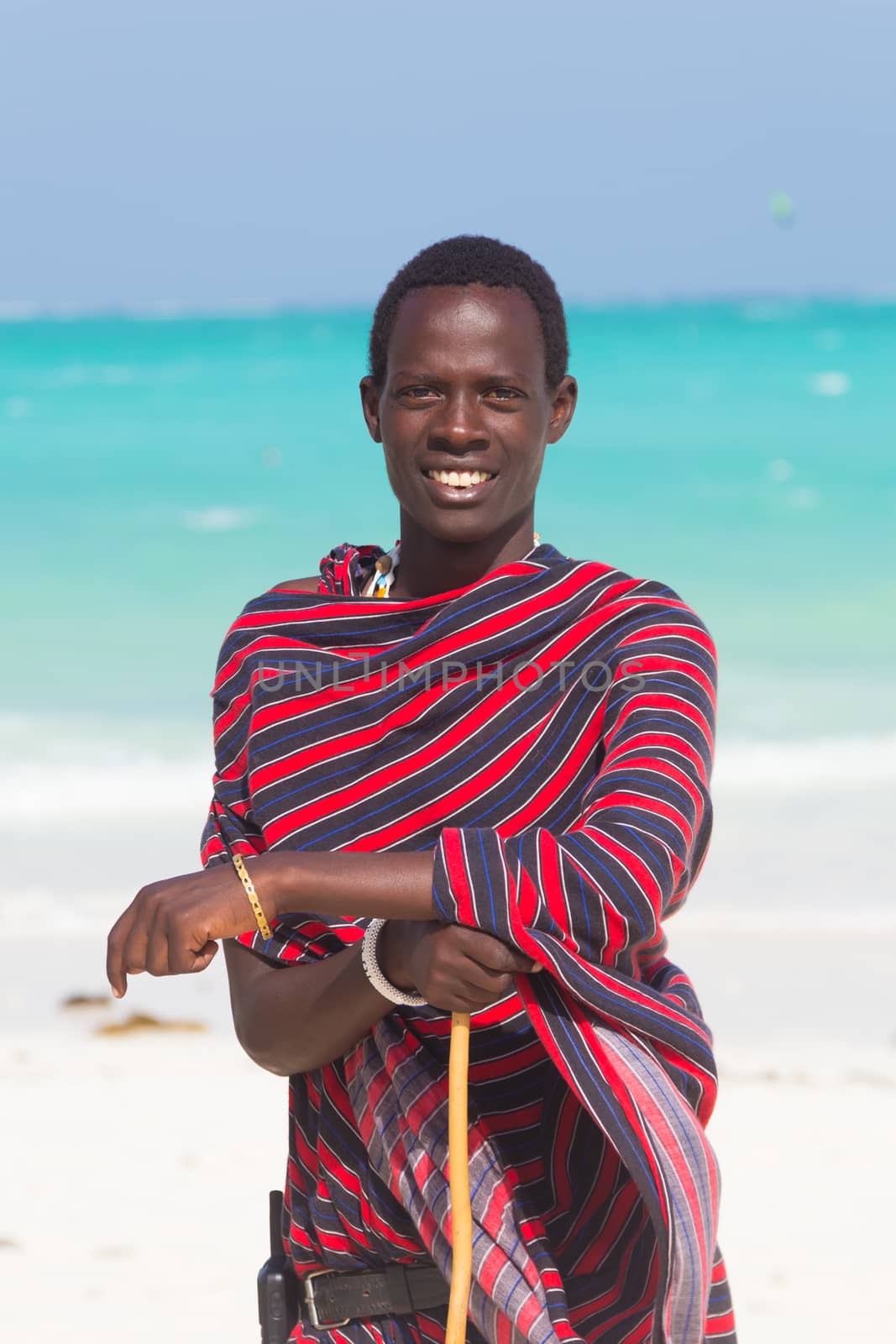 Traditonaly dressed masai black man on Paje beach. Maasai warrior on picture perfect tropical sandy beach on Zanzibar, Tanzania, East Africa.