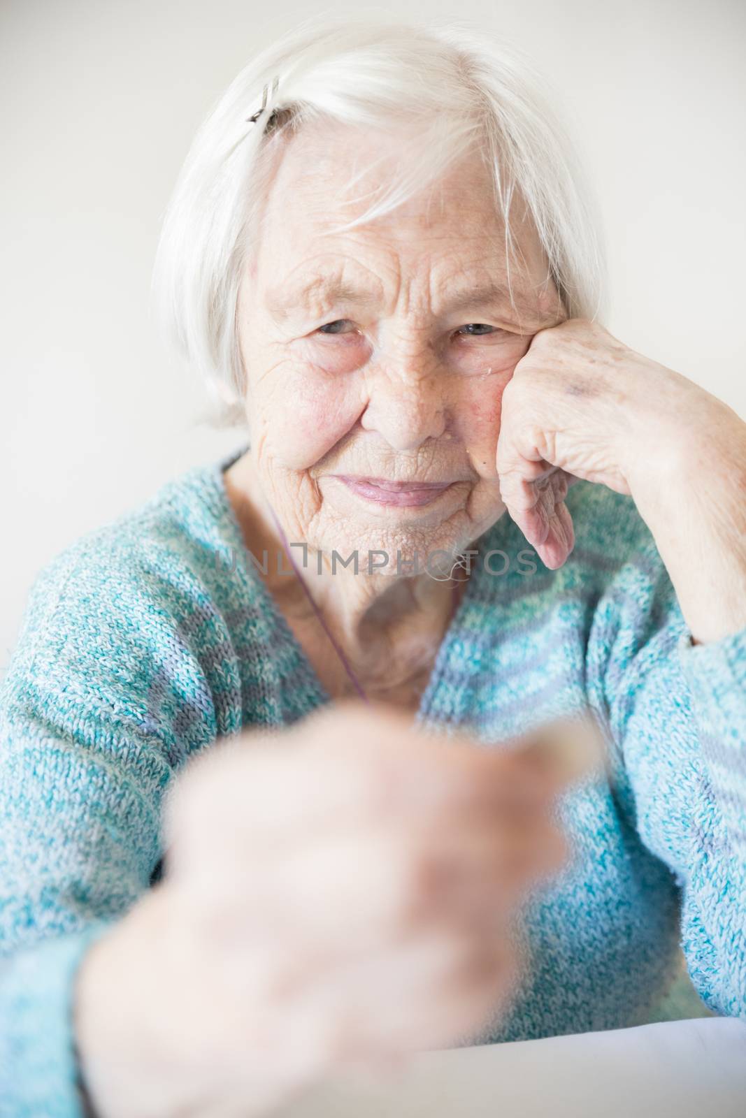 Sad elderly woman sitting at the table at home and looking miserably at only remaining coin from pension in her hand. Unsustainability of social transfers and pension system. Selective focus image.