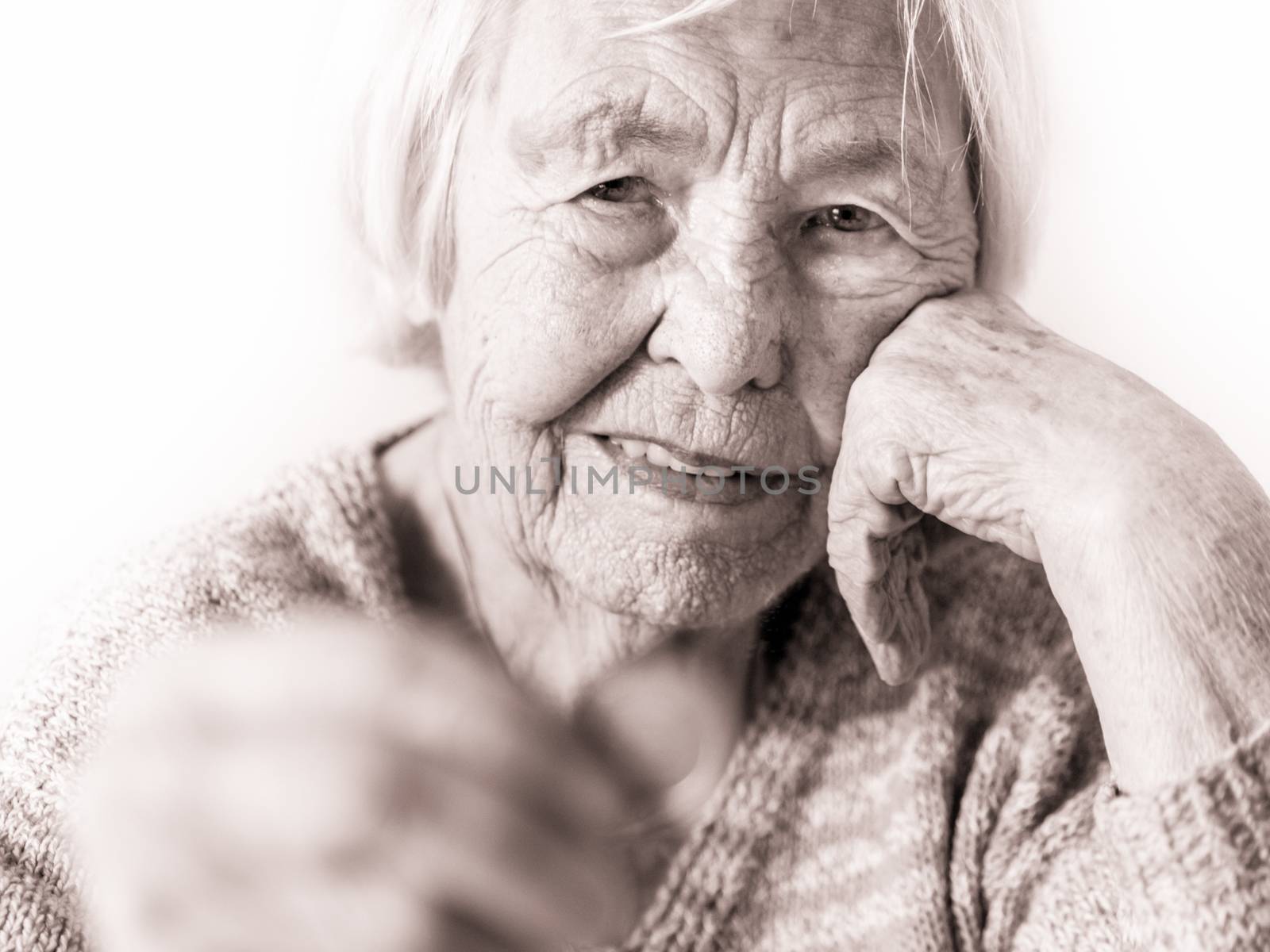 Portrait of sad elderly woman sitting at table at home and looking miserably at only remaining coin from pension in hand. Unsustainability of social transfers and pension system. Selective focus.