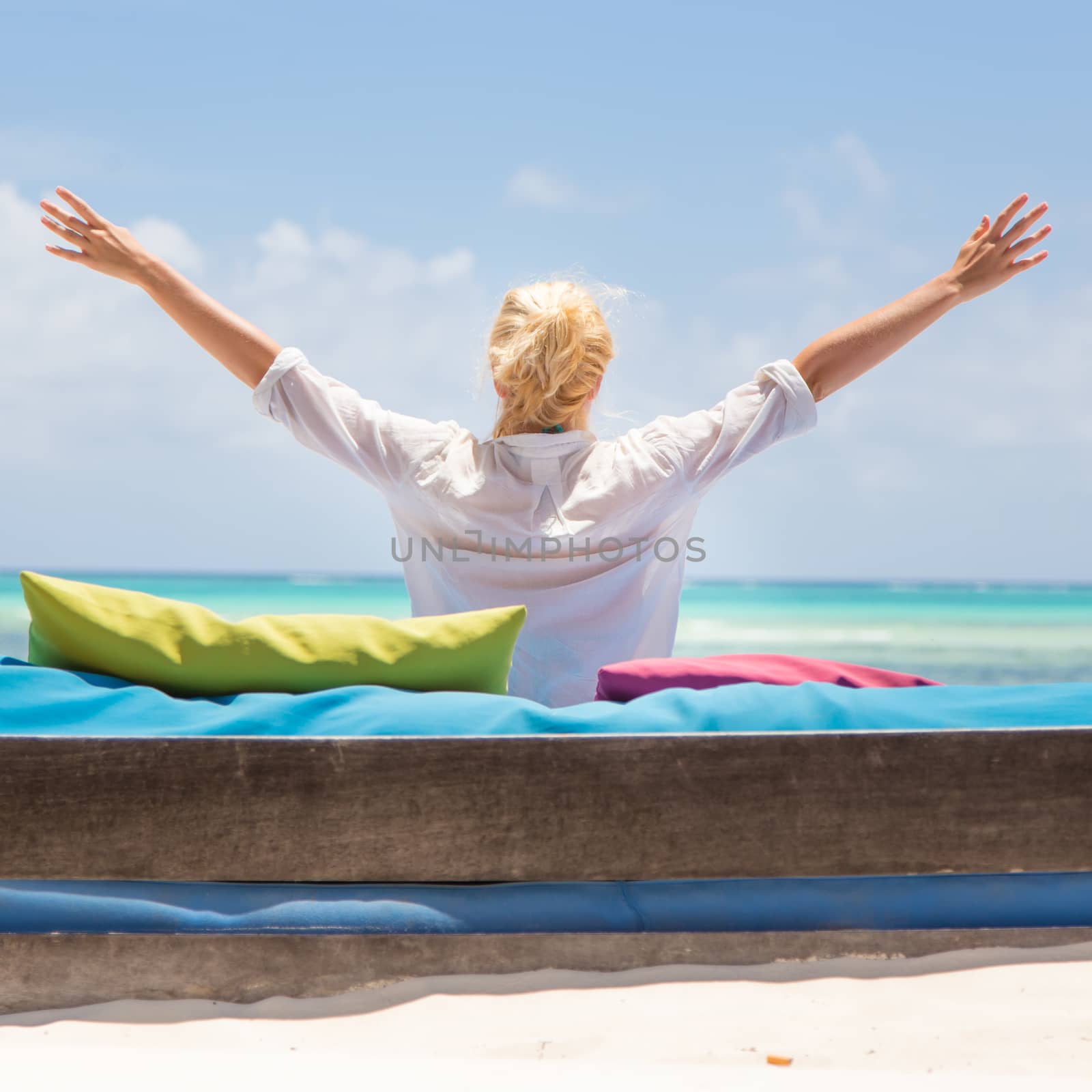 Relaxed woman in luxury lounger, arms rised, enjoying summer vacations on beautiful beach. by kasto