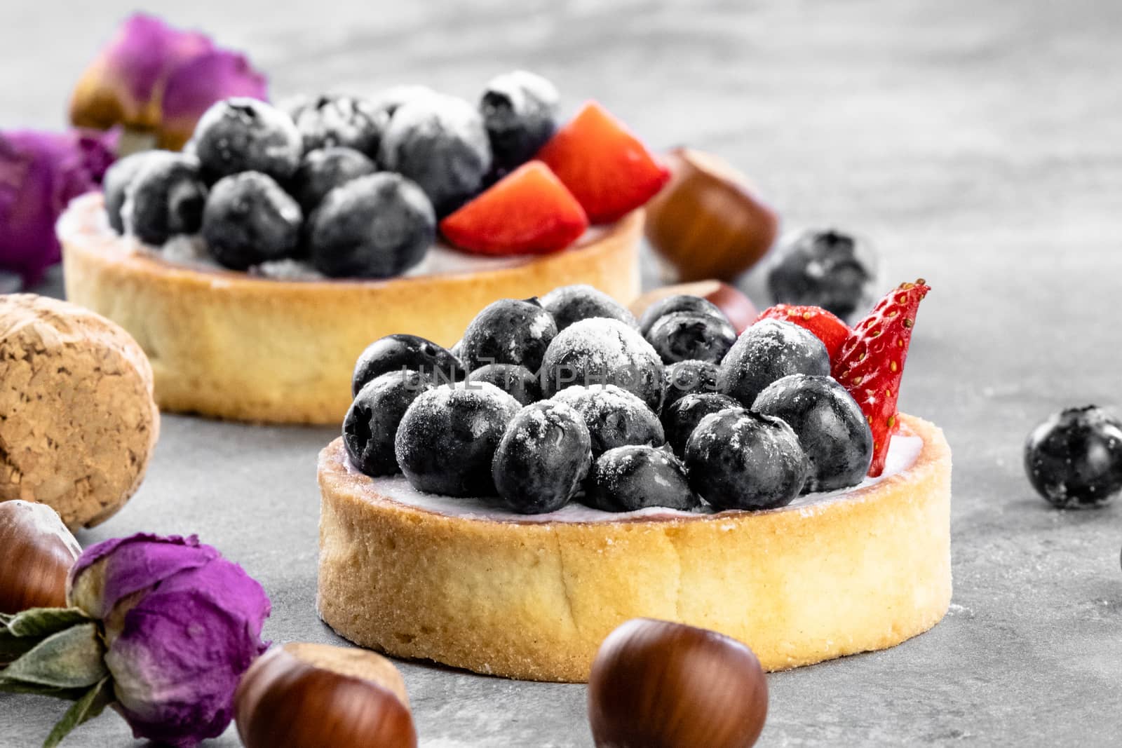 Blueberry and strawberry shortcake. There are hazelnuts, roses and wine corks on the table. Stone gray background.