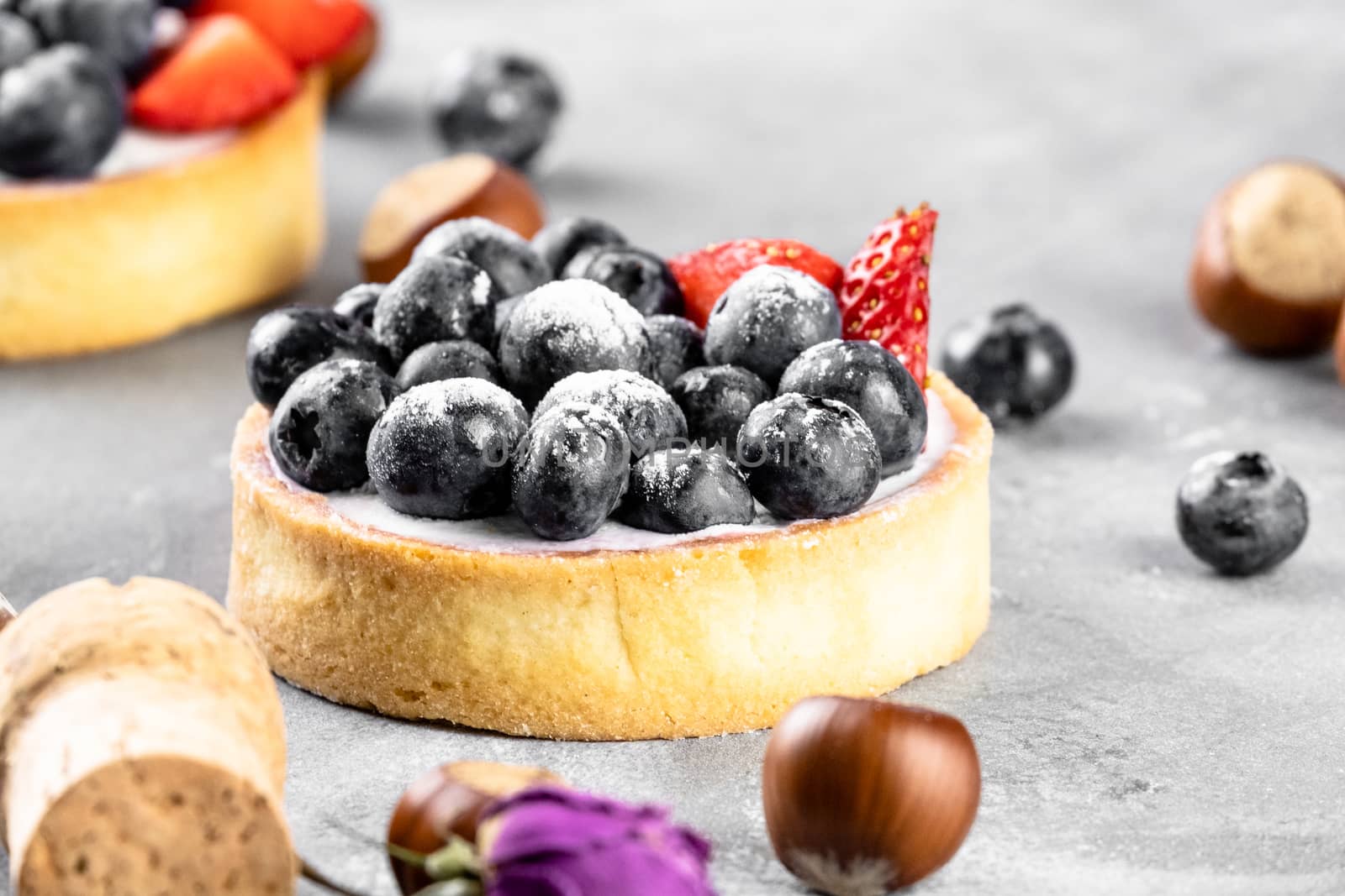 Blueberry and strawberry shortcake. There are hazelnuts, roses and wine corks on the table. Stone gray background.