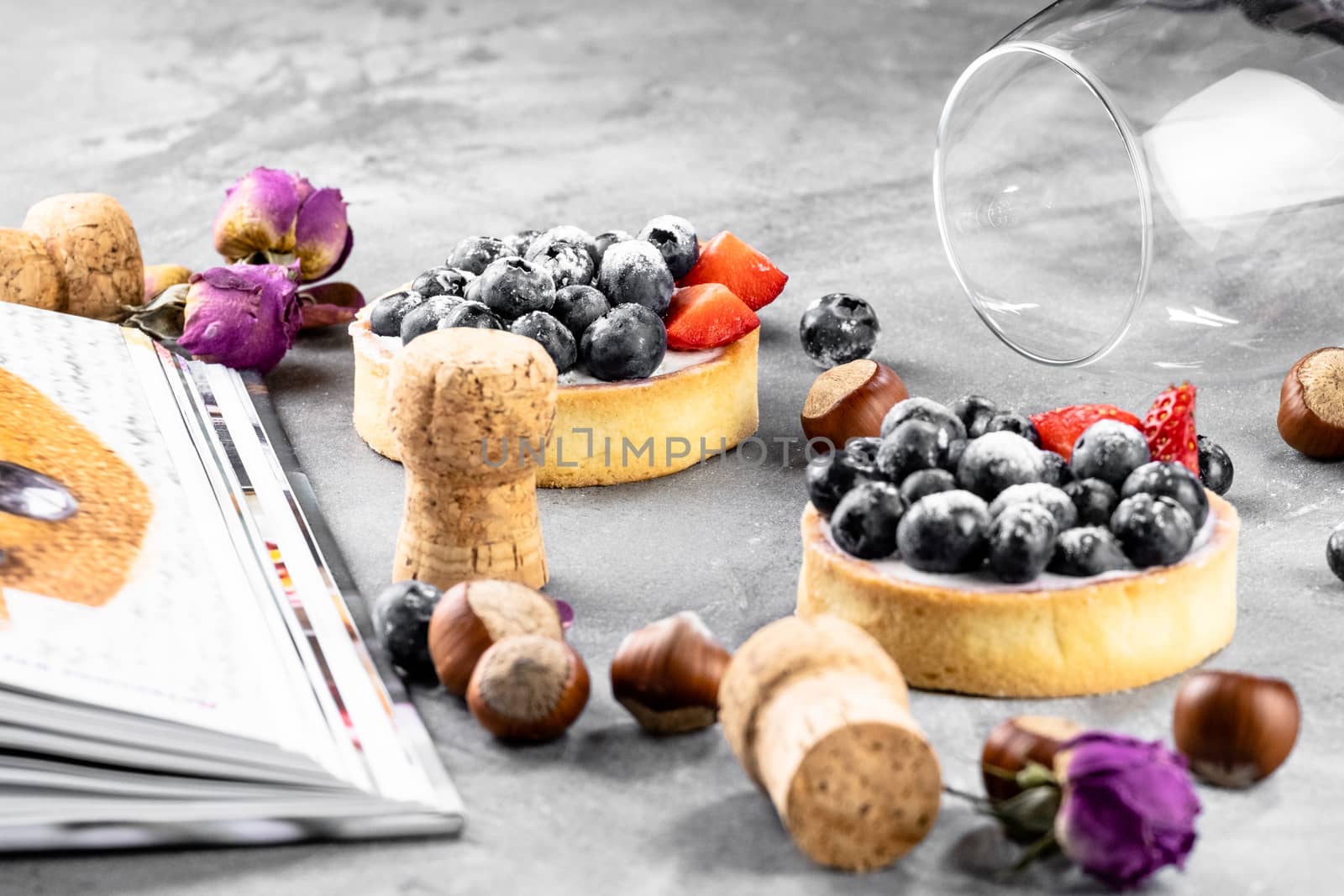 Blueberry and strawberry shortcake. There are hazelnuts, roses and wine corks on the table. Stone gray background.