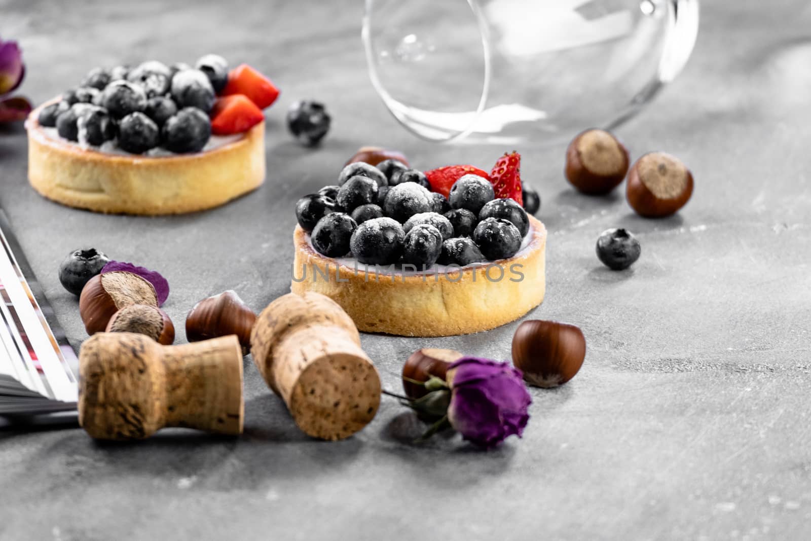 Blueberry and strawberry shortcake. There are hazelnuts, roses and wine corks on the table. Stone background. by rdv27