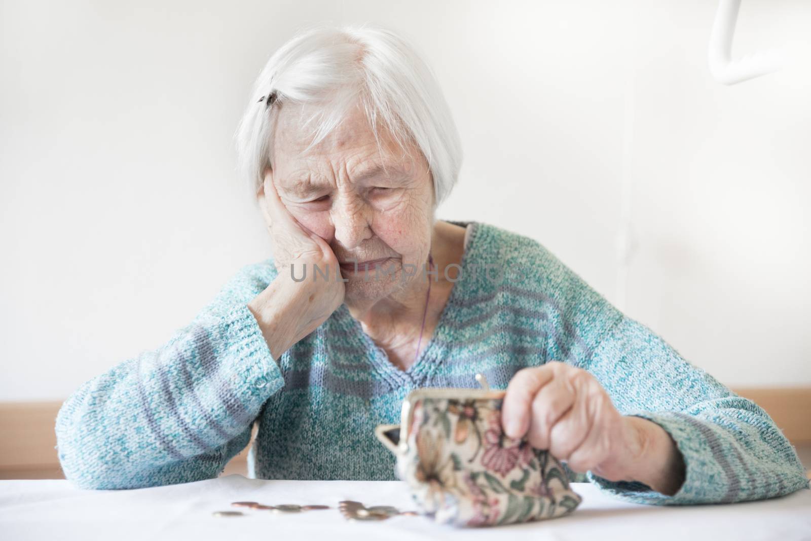 Concerned elderly 96 years old woman sitting at table at home and counting remaining coins from pension in her wallet after paying bills. Unsustainability of social transfers and pension system.