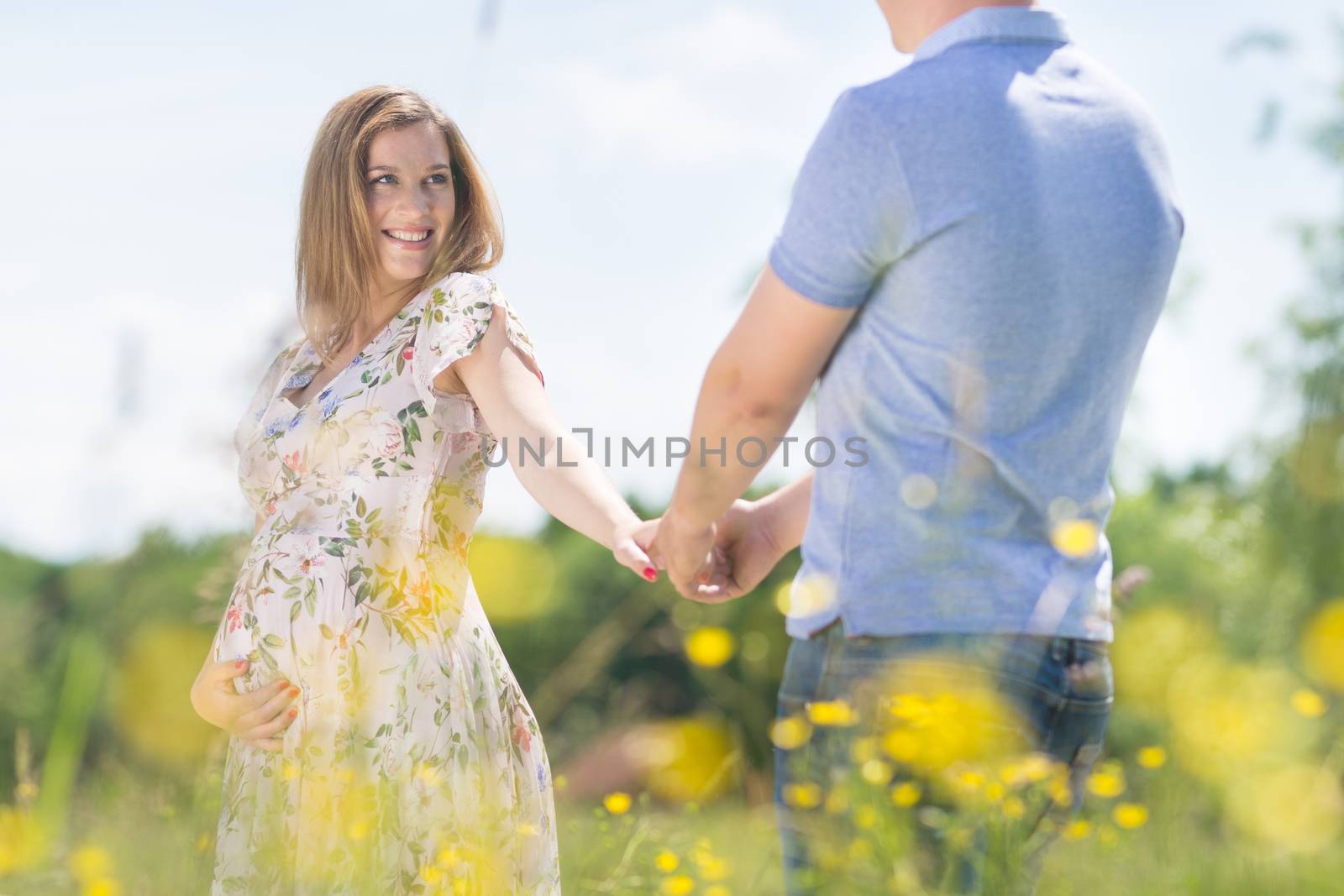 Young happy pregnant couple in love holding hands, relaxing in meadow. Concept of love and family creation.