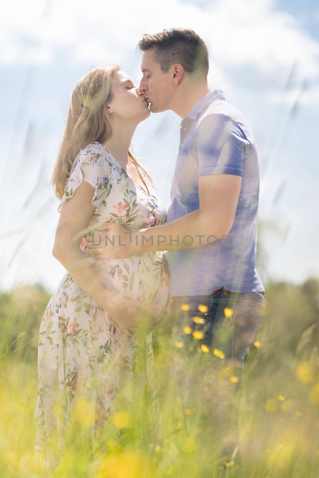 Young happy pregnant couple in love holding hands, relaxing in meadow. by kasto