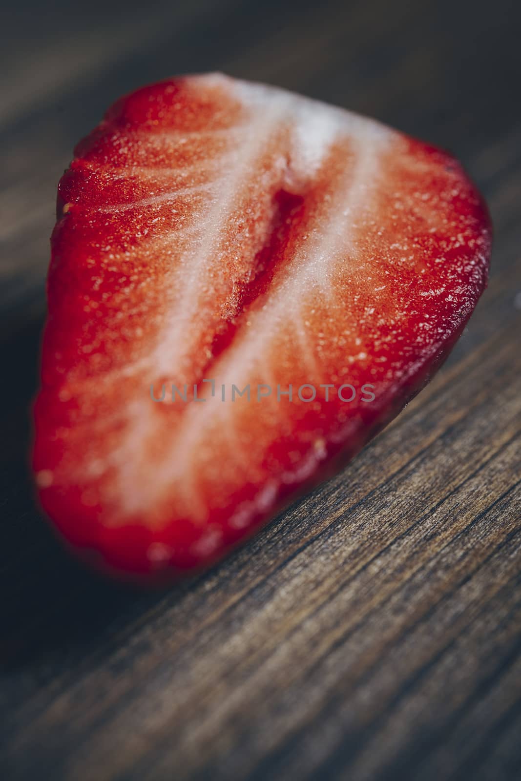 vertical photo of a half strawberry on a wooden background in rustic style